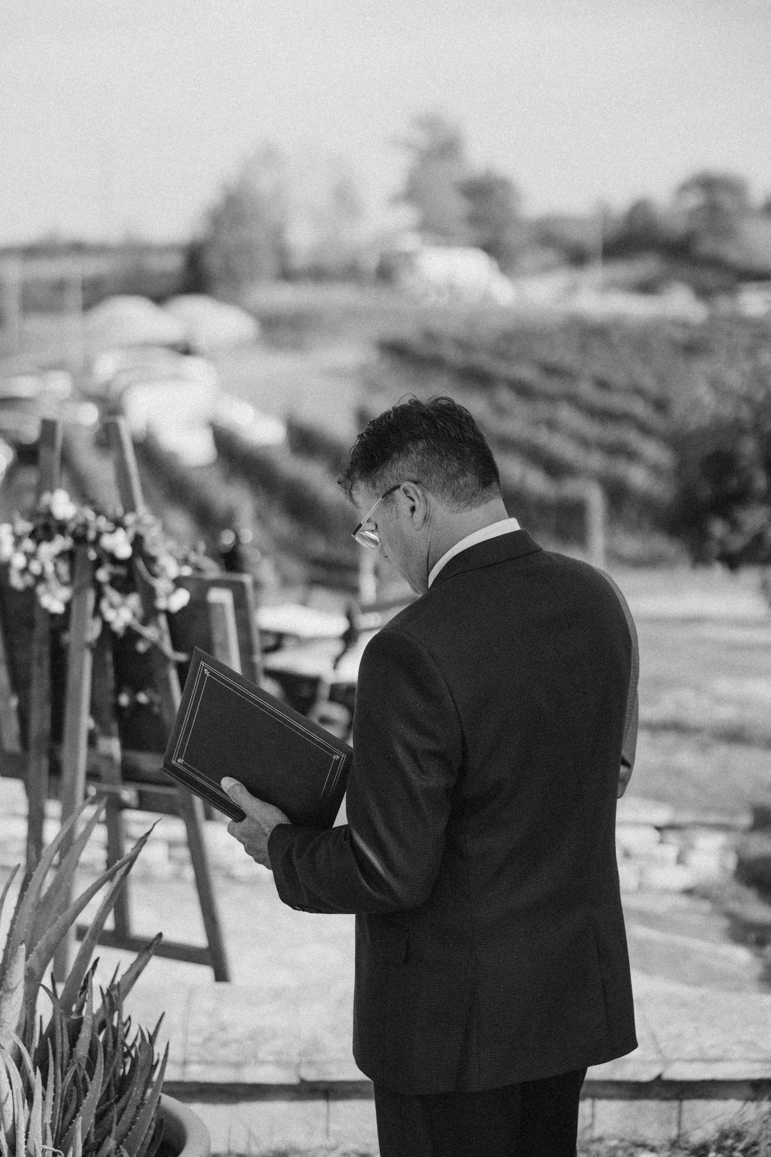 Wedding photographer in formal attire taking pictures during an outdoor ceremony.