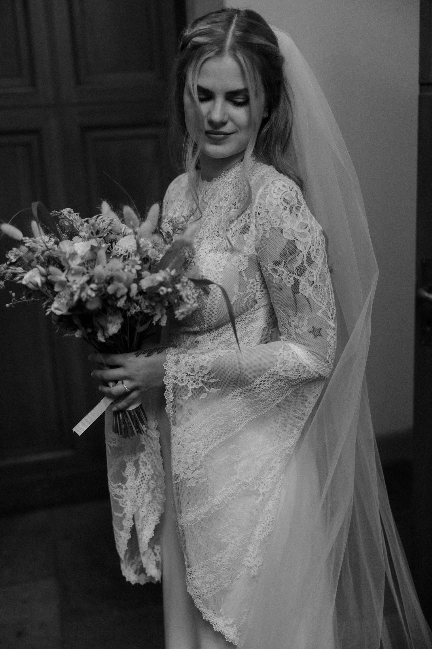 Elegant wedding dress with lace details and flowing veil captured in black and white photography.