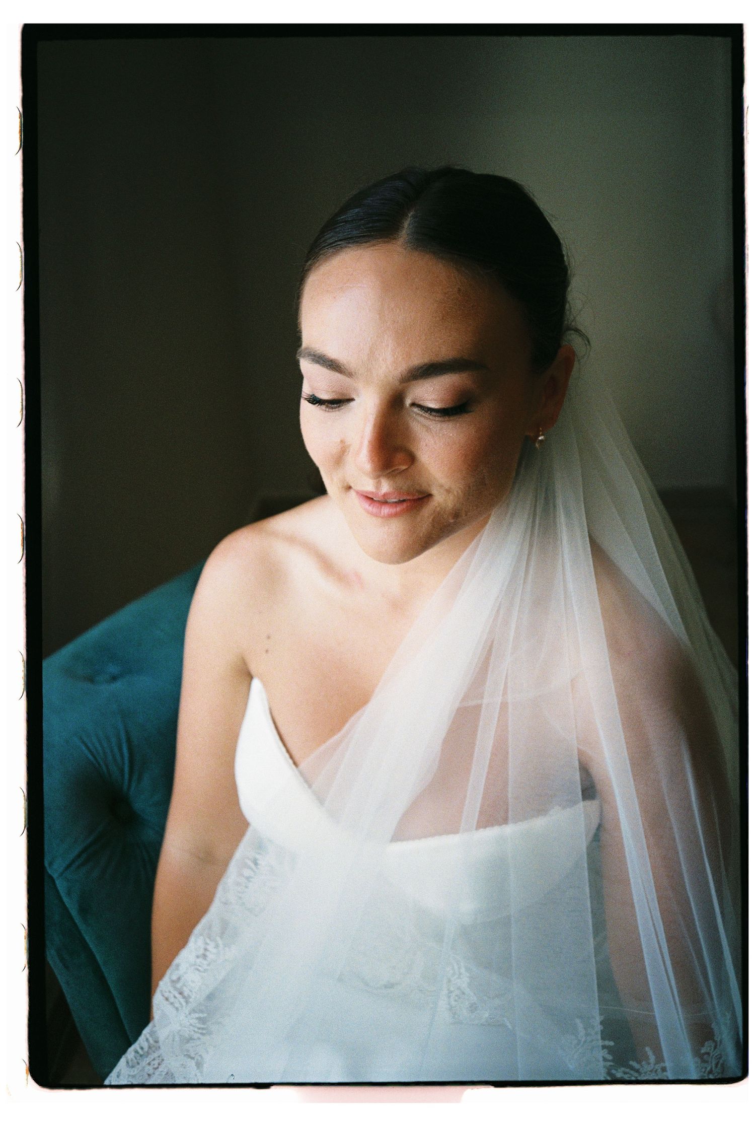 Bride with elegant updo and lace veil looks down softly in natural light.