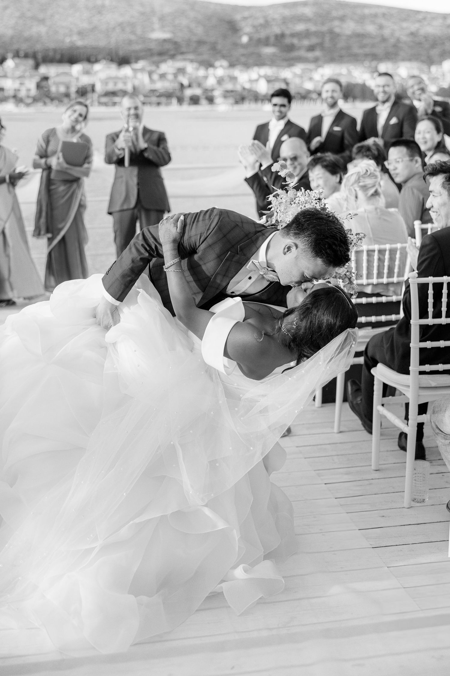 Groom dips bride for romantic kiss at outdoor wedding ceremony in black and white photo.