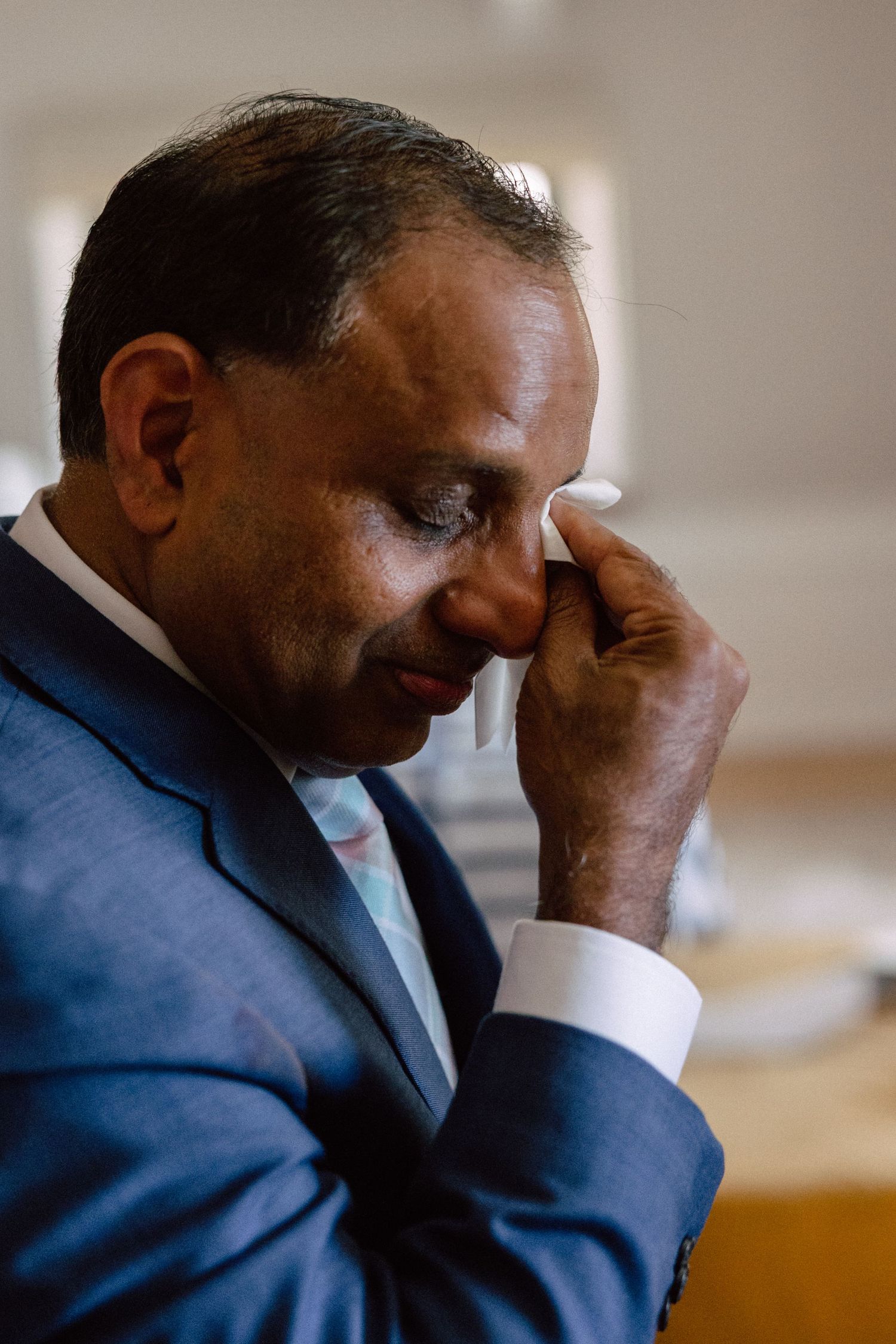 Emotional man in blue suit wiping tears from his eye during a wedding ceremony.