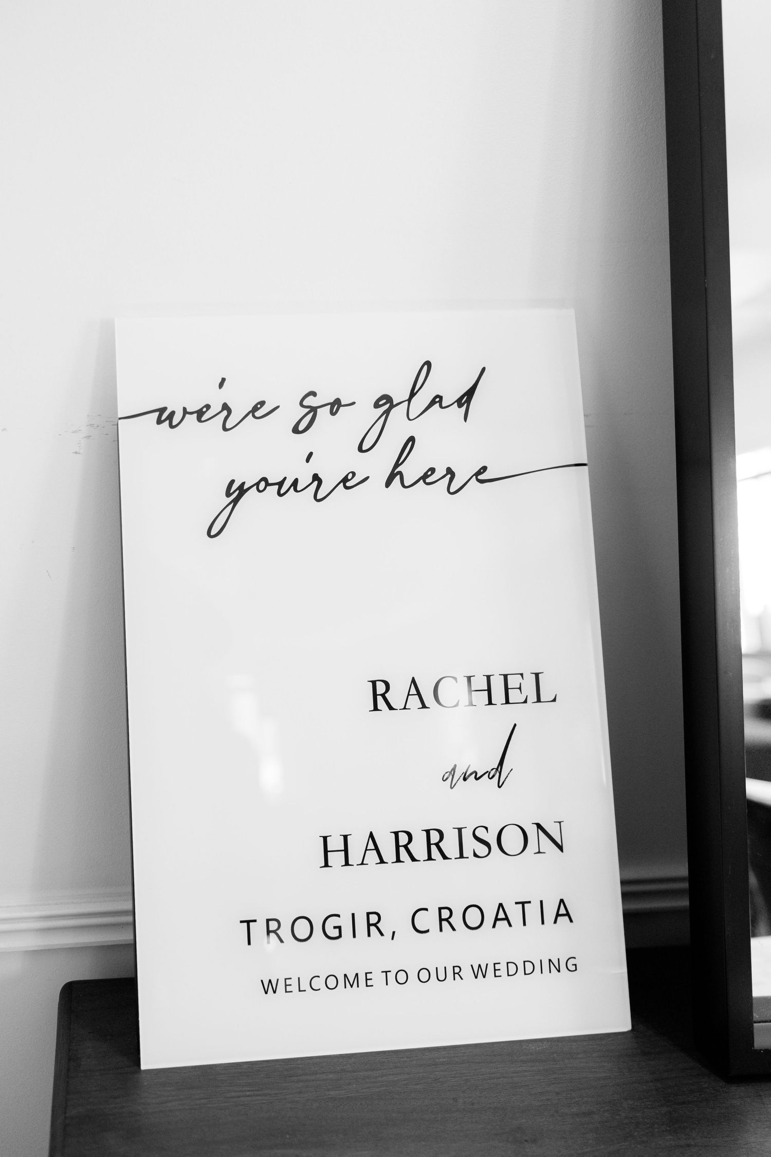 Black and white wedding welcome sign for Rachel and Harrison in Trogir, Croatia reading we're so glad you're here.