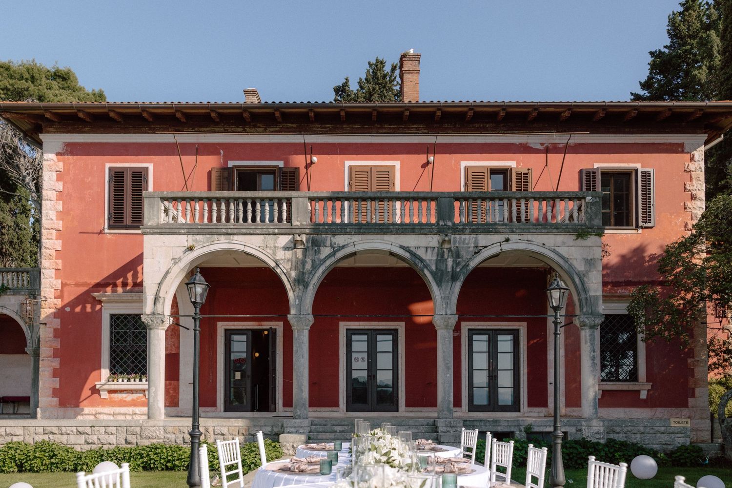 Mediterranean villa facade with ornate pink walls and traditional balconies overlooking the coastline.