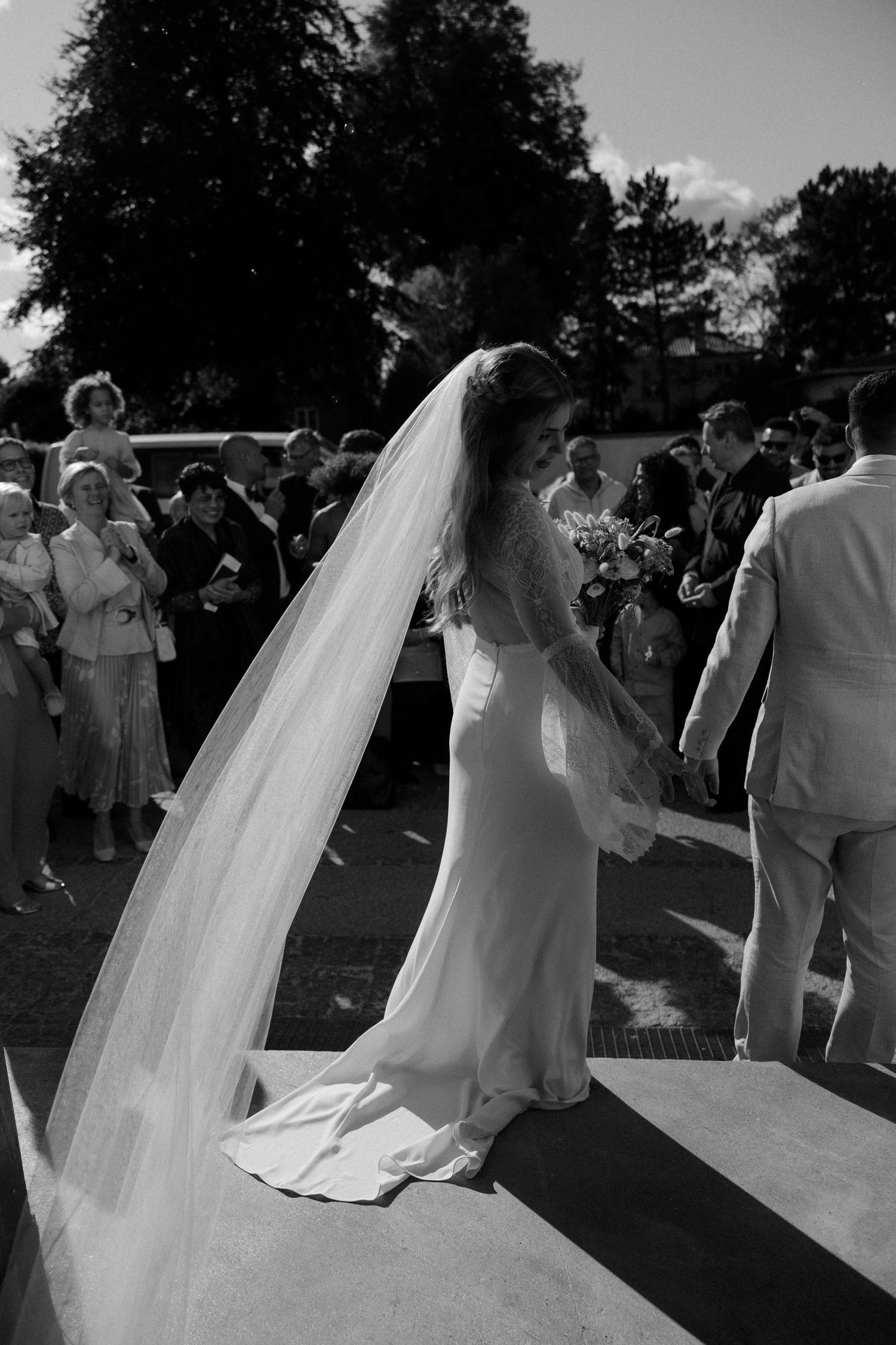 Bride in flowing wedding gown and long veil descending outdoor steps at ceremony.