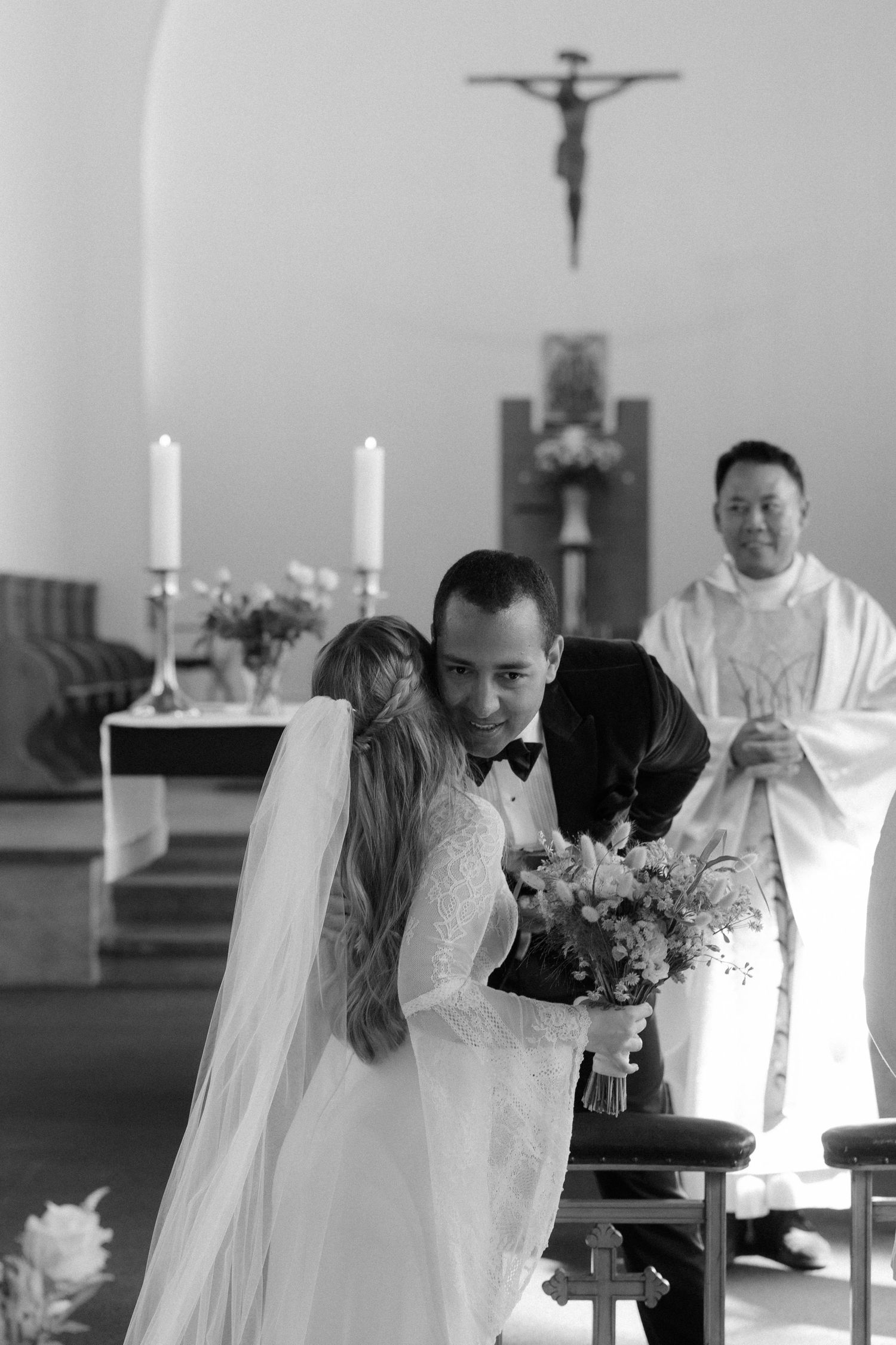 Church ceremony with lit candles and white floral arrangements at the altar.