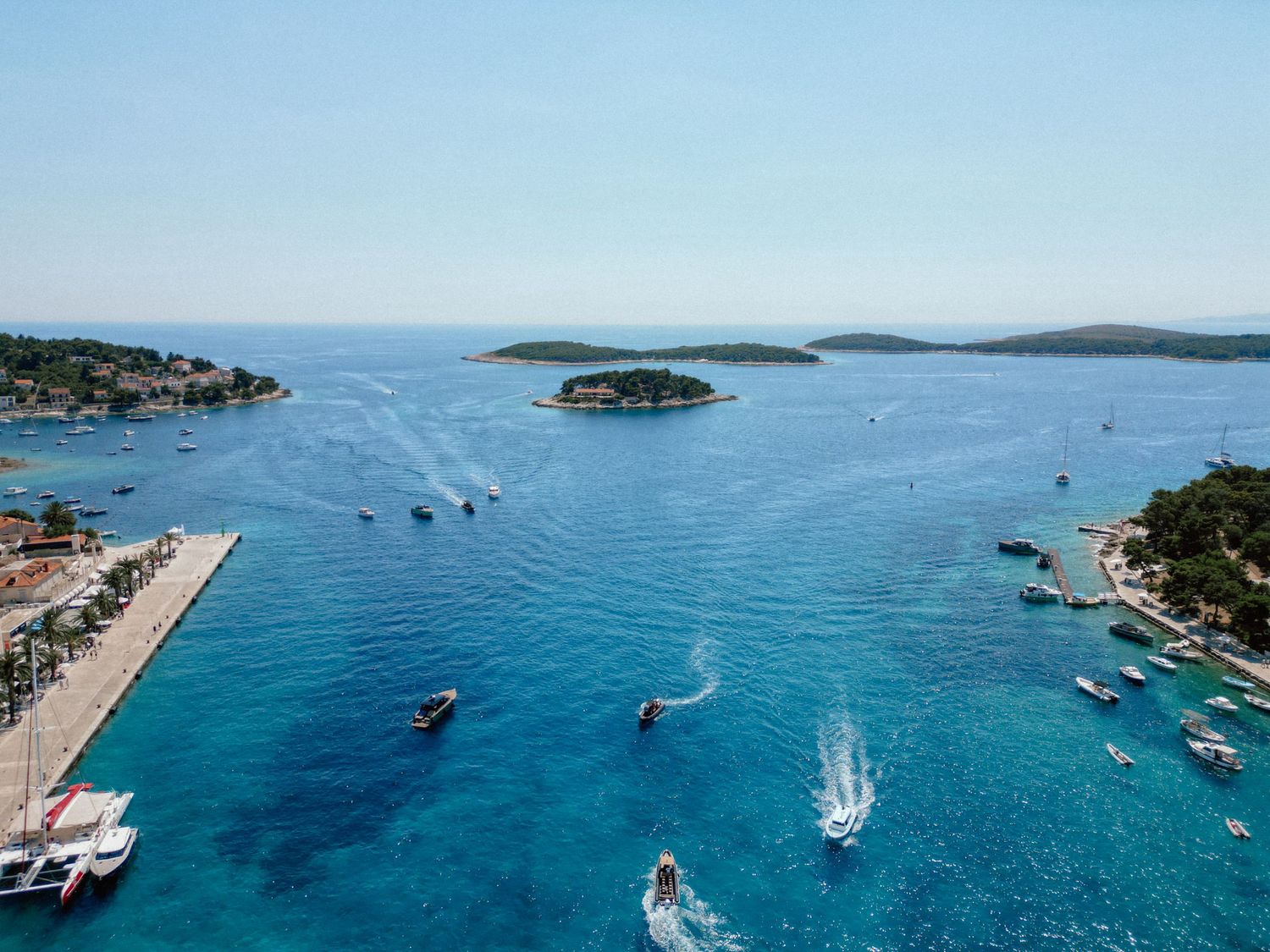 Aerial view of crystal-clear turquoise waters near Hvar, Croatia, with boats sailing around lush green islands.