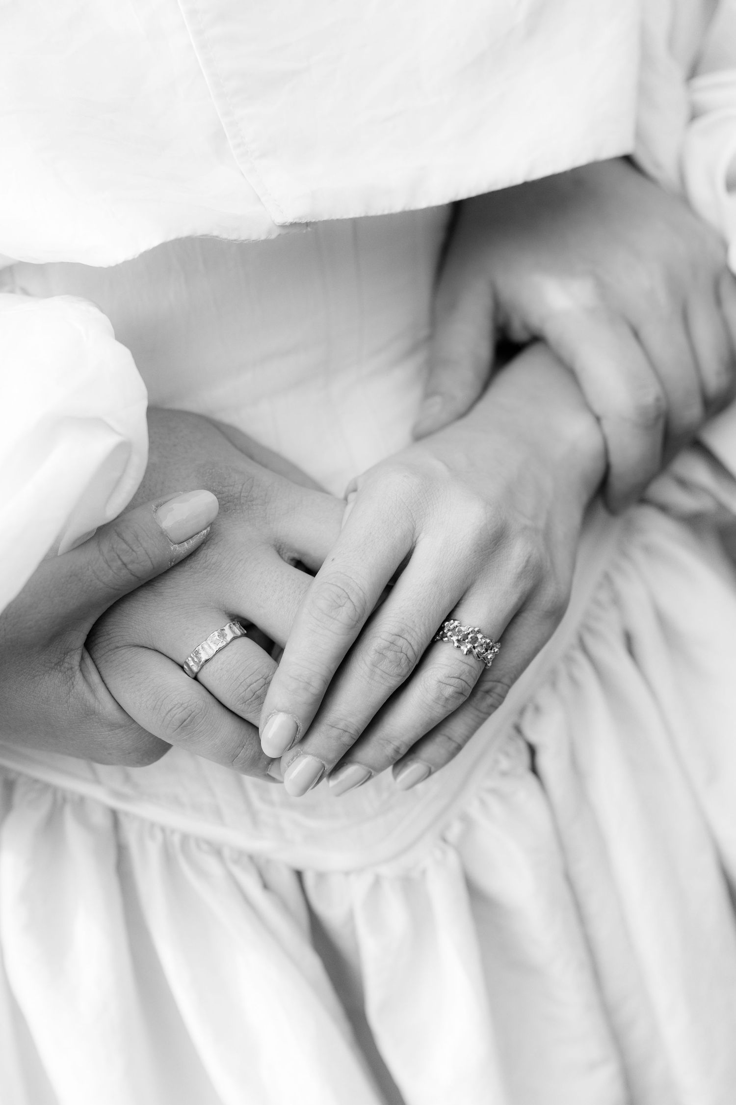 Close-up of hands with wedding rings resting on white fabric.