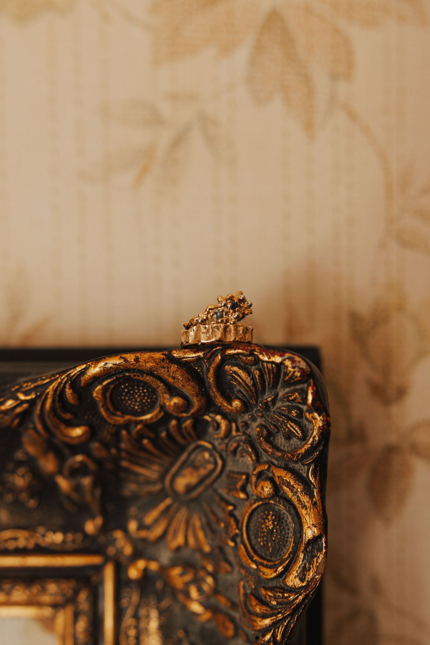 Ornate gold baroque frame detail with floral patterns against beige wall.