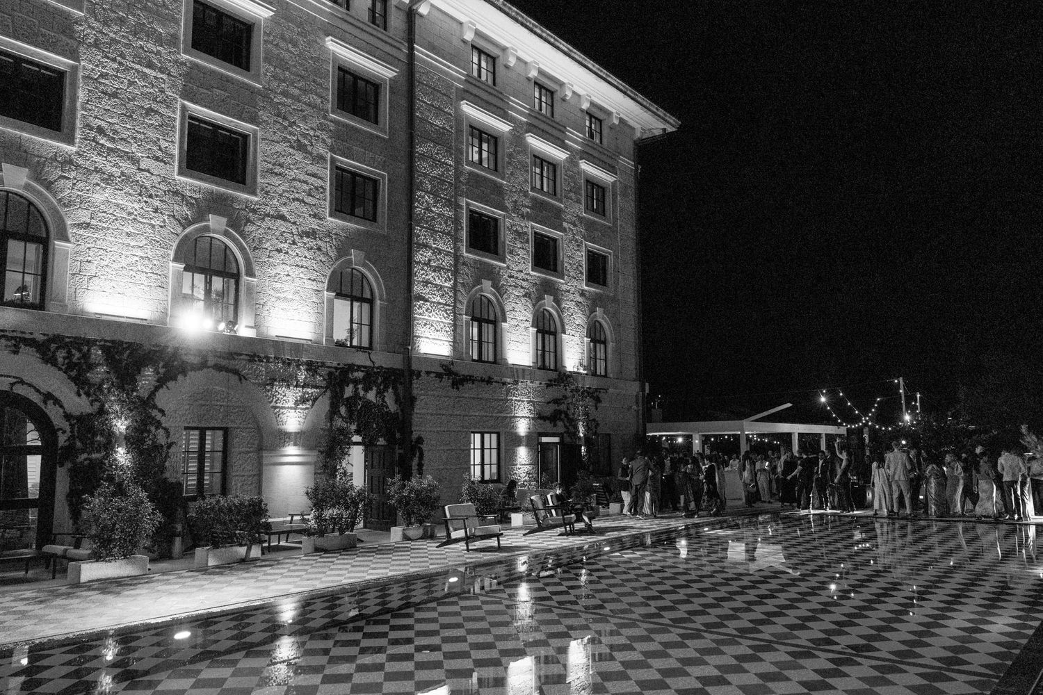 Black and white nighttime exterior shot of an illuminated historic stone building hosting a wedding reception.