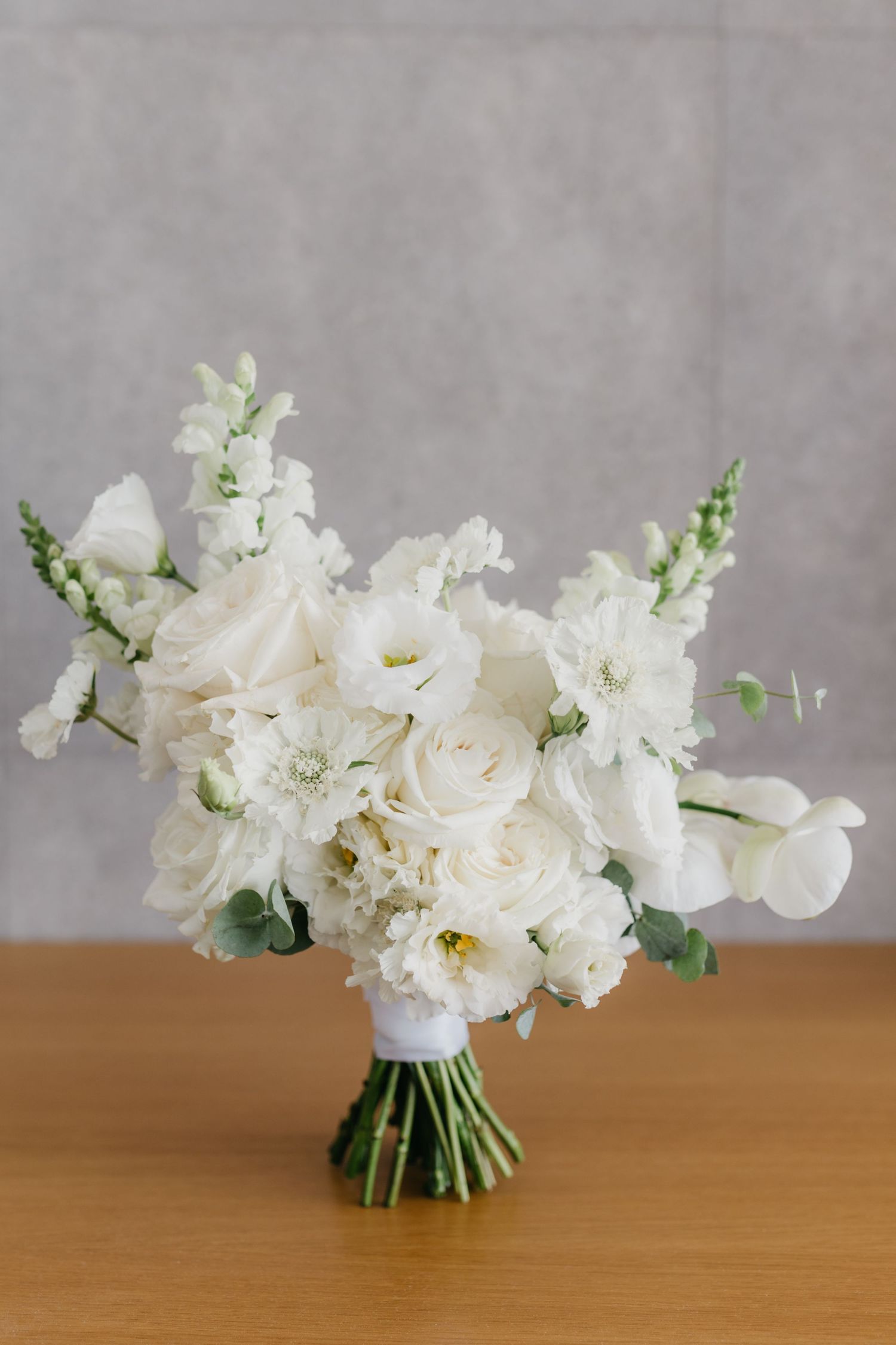 Stunning white bridal bouquet with roses and delicate flowers on wooden surface.