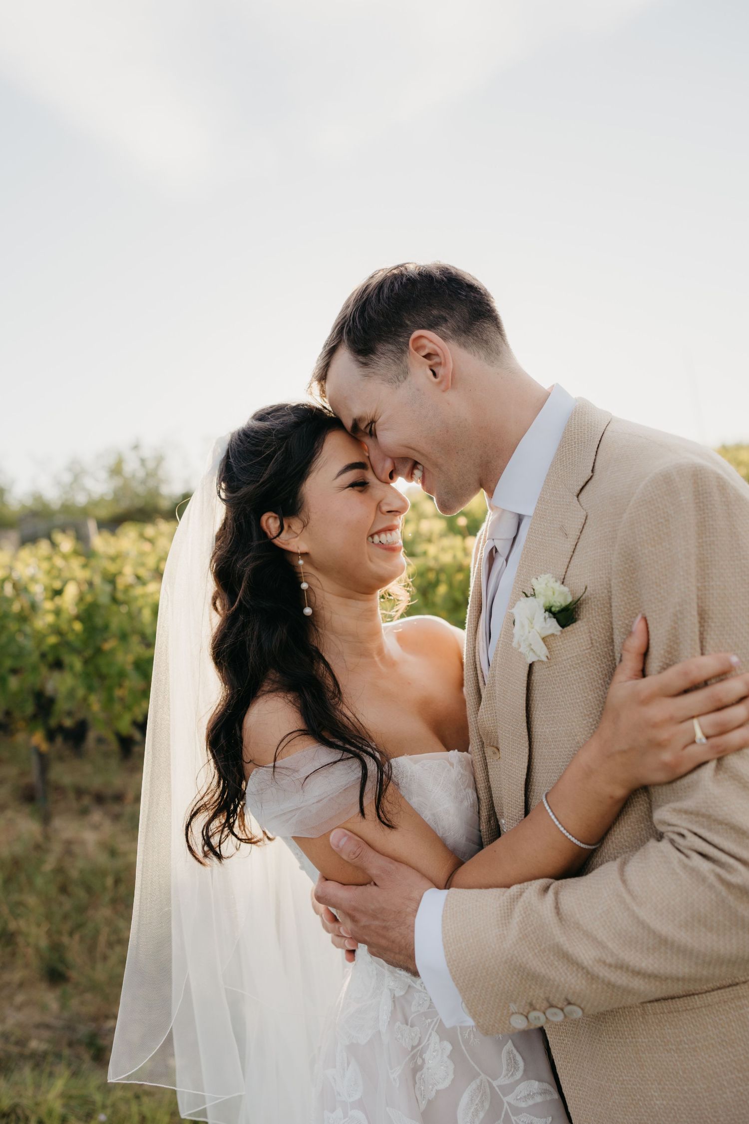 Couple embraces and laughs together against backdrop of vineyard rows in Italy.