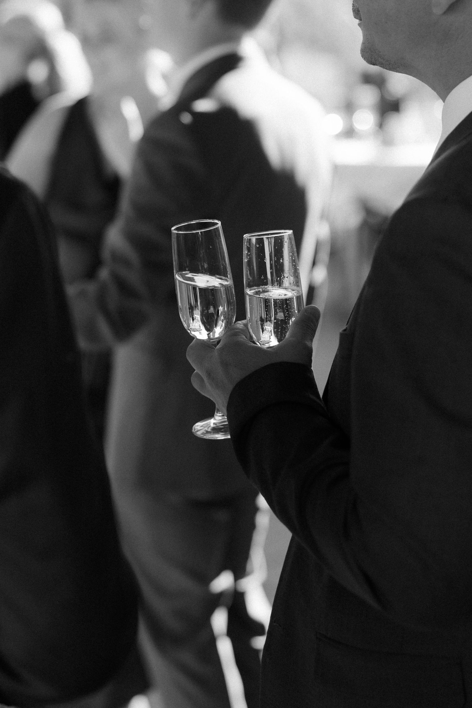 Elegant black and white photo of champagne glasses being held at a formal event.