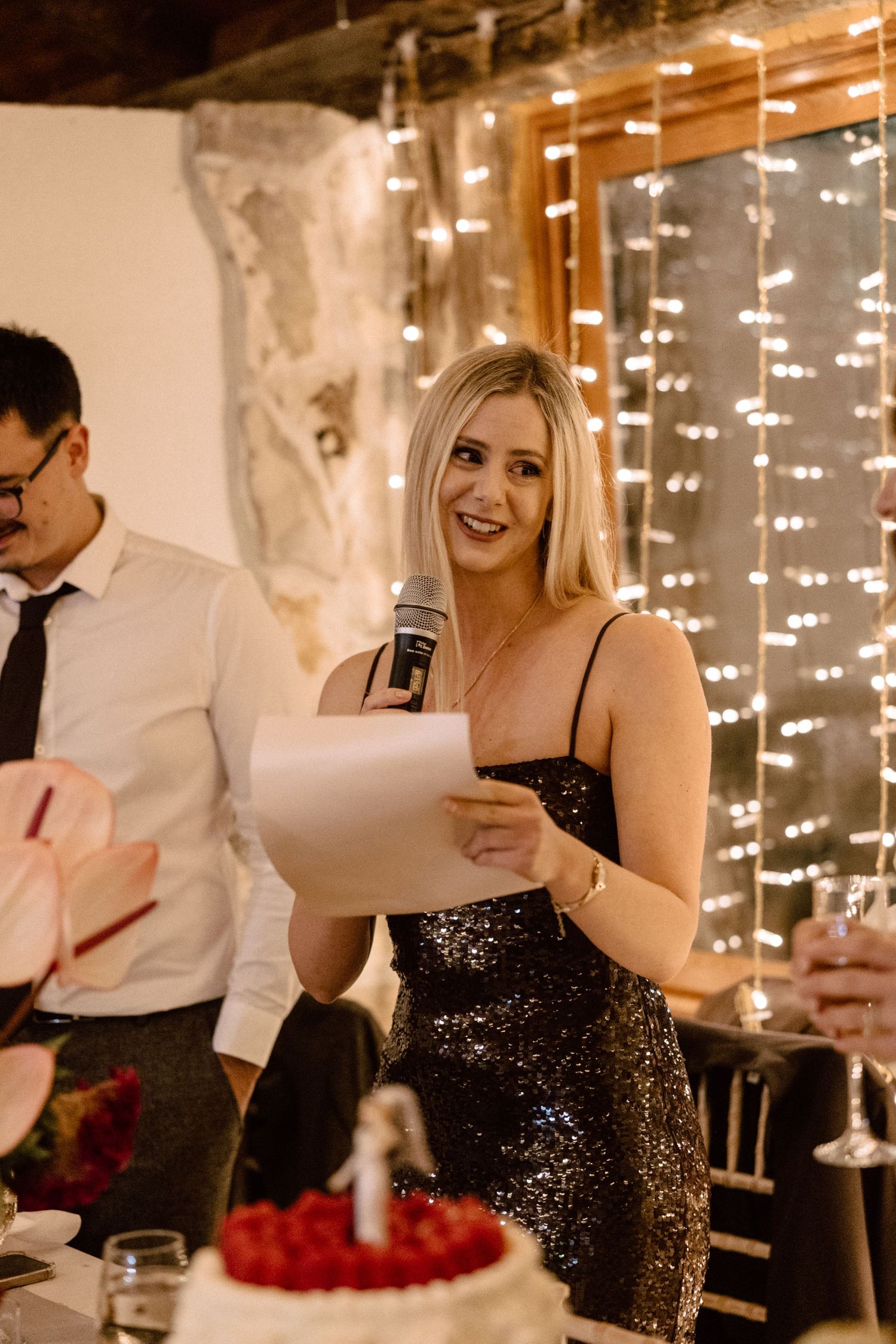 A wedding guest in a sparkly dress gives a speech at the reception.