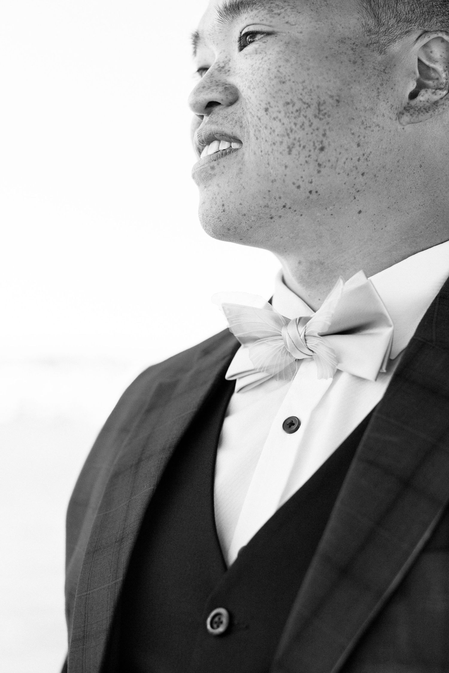 Black and white close-up portrait of a smiling groom wearing a bow tie and suit jacket.