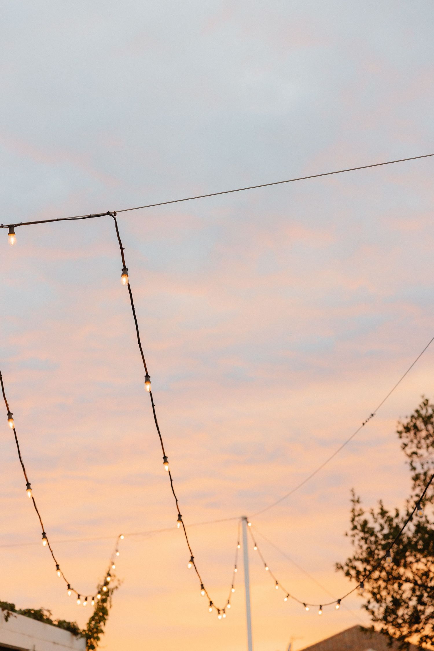 String lights hang against a pastel pink and blue sunset sky at wedding venue.