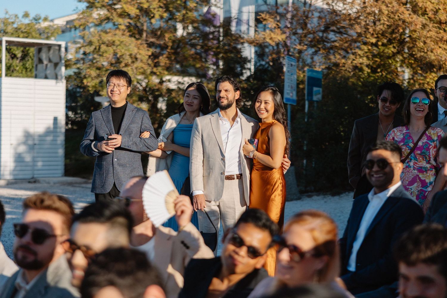 Smiling wedding guests standing outdoors during a sunny wedding reception celebration.