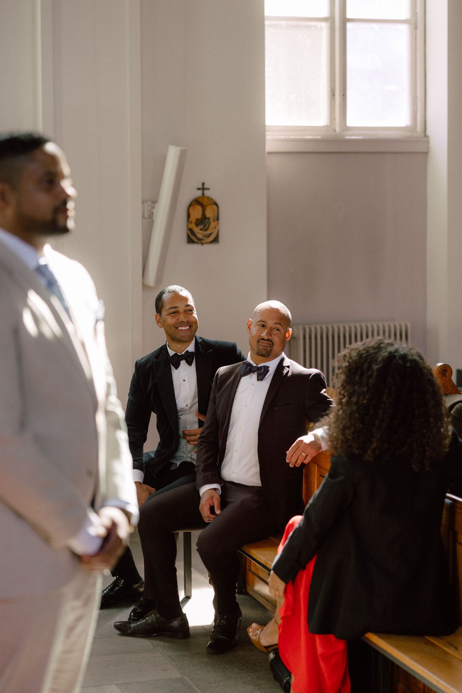 Wedding guests seated in white church pews during a joyful ceremony celebration.