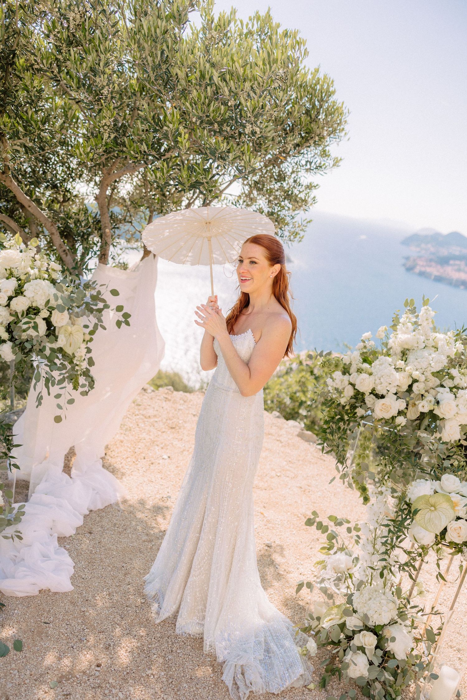 A bride in white dress enjoys moments in a sun-drenched garden with white floral decorations.