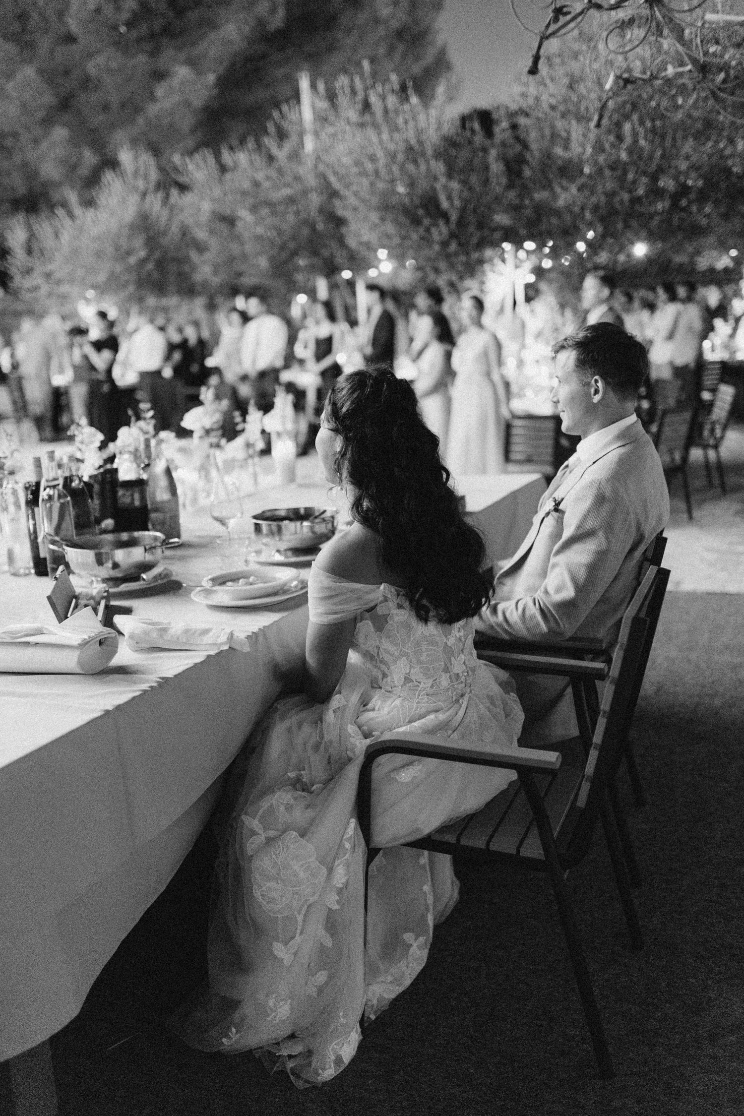 Evening wedding reception scene with guests seated at tables under twinkling lights.