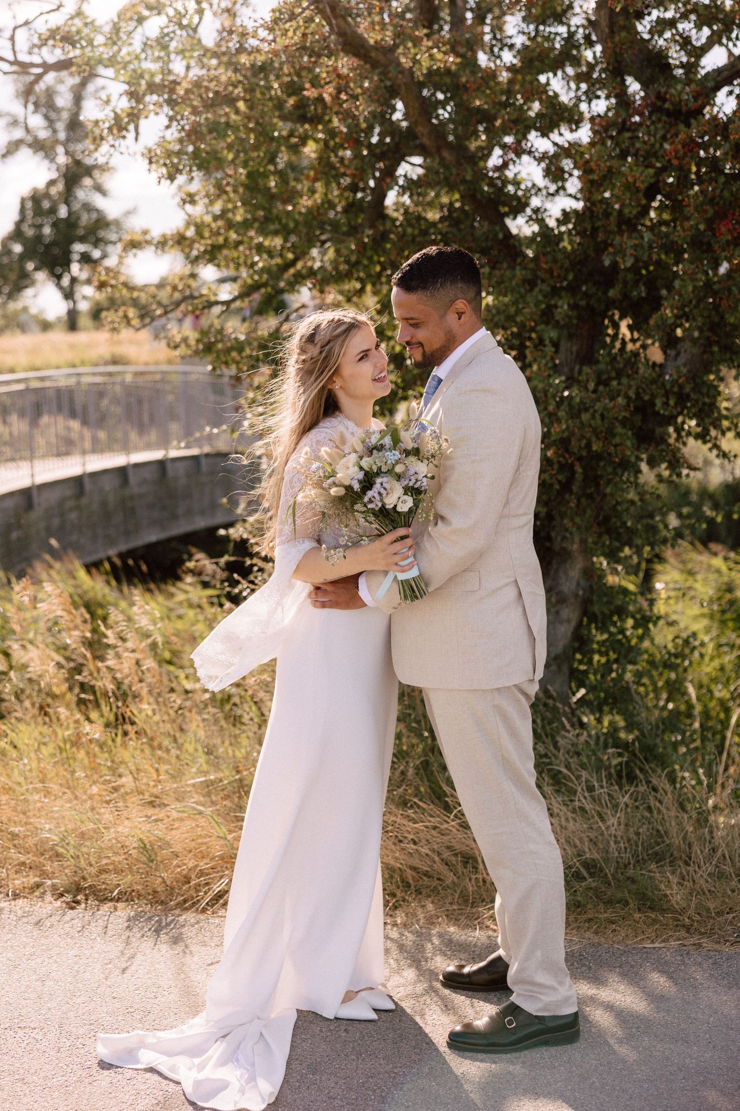 Romantic portrait of couple in wedding attire embracing on rustic path with sunset lighting.