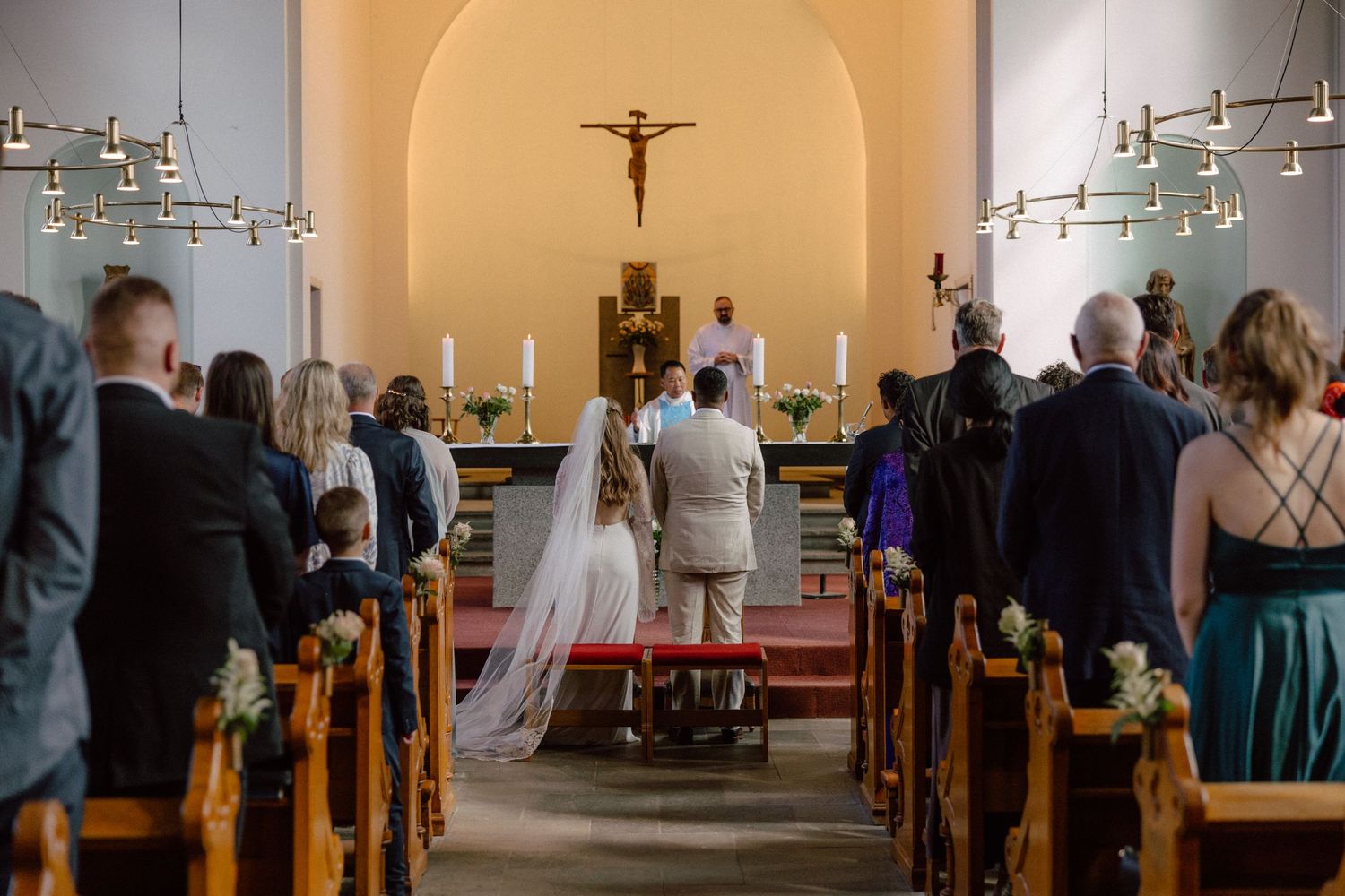 Wide angle view of church interior with sunlit windows and gathered wedding guests.