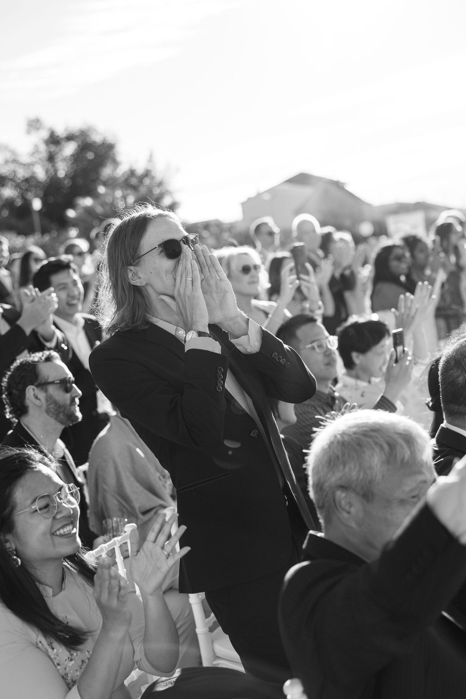 Wedding guests clapping and cheering with emotion during an outdoor ceremony in black and white photography.