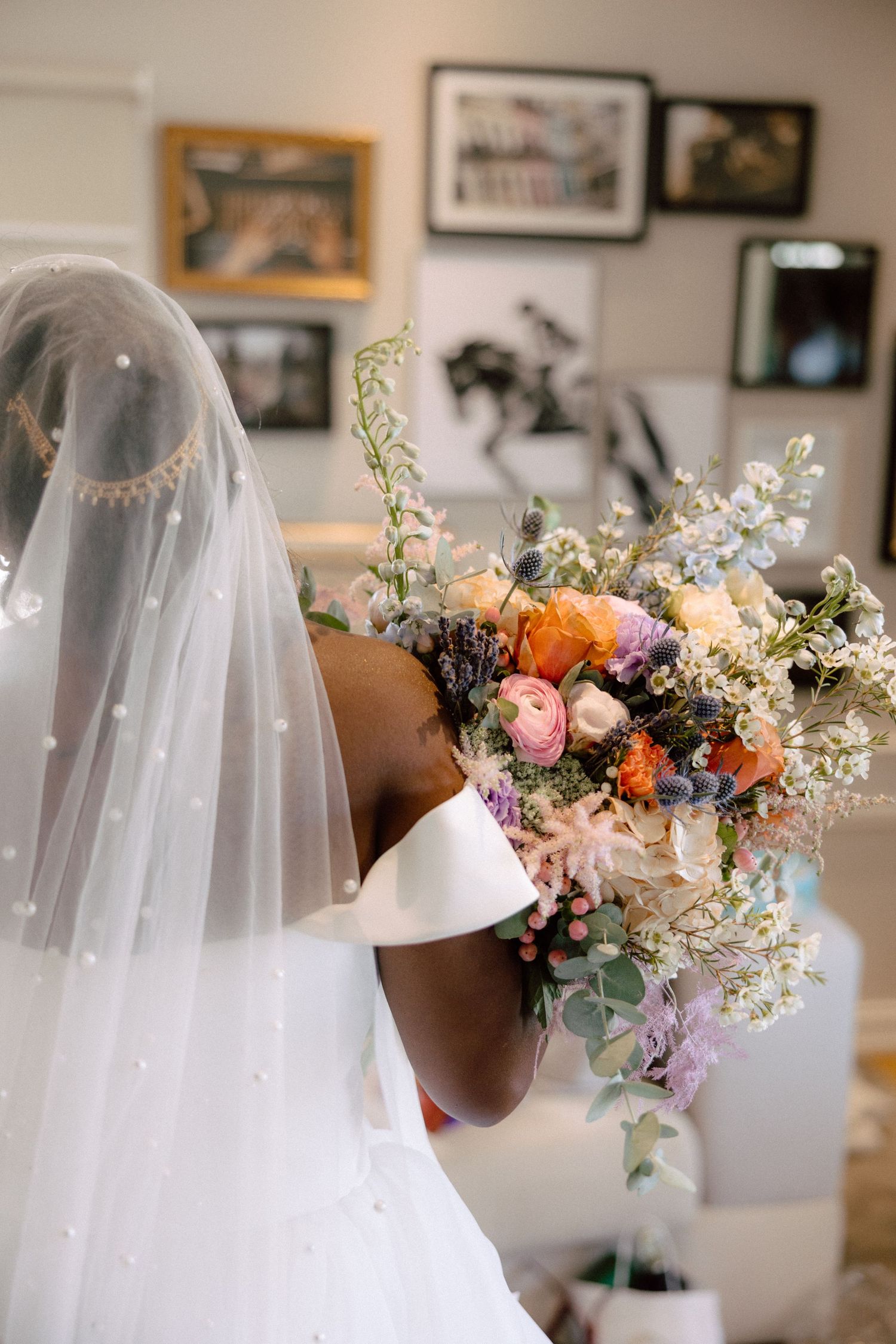 Bride in pearl-dotted veil holding a colorful bridal bouquet with ranunculus and wildflowers.