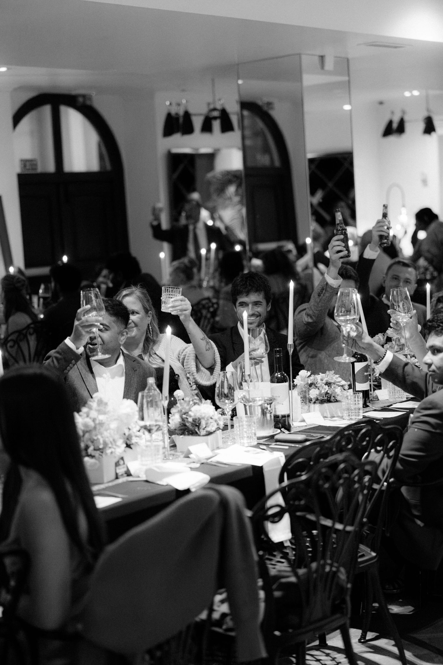 Black and white photo of elegantly dressed guests raising glasses in a toast at a formal dinner reception.