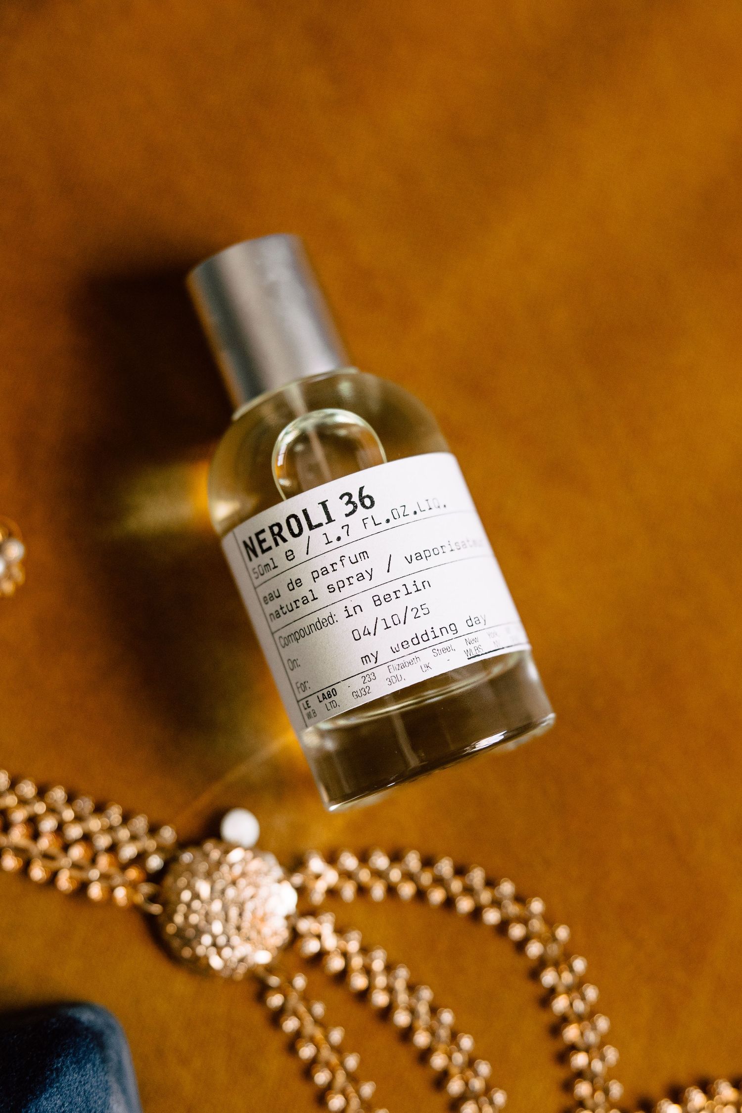 Le Labo Neroli 36 perfume bottle with gold beaded jewelry on a warm golden surface for a wedding day.