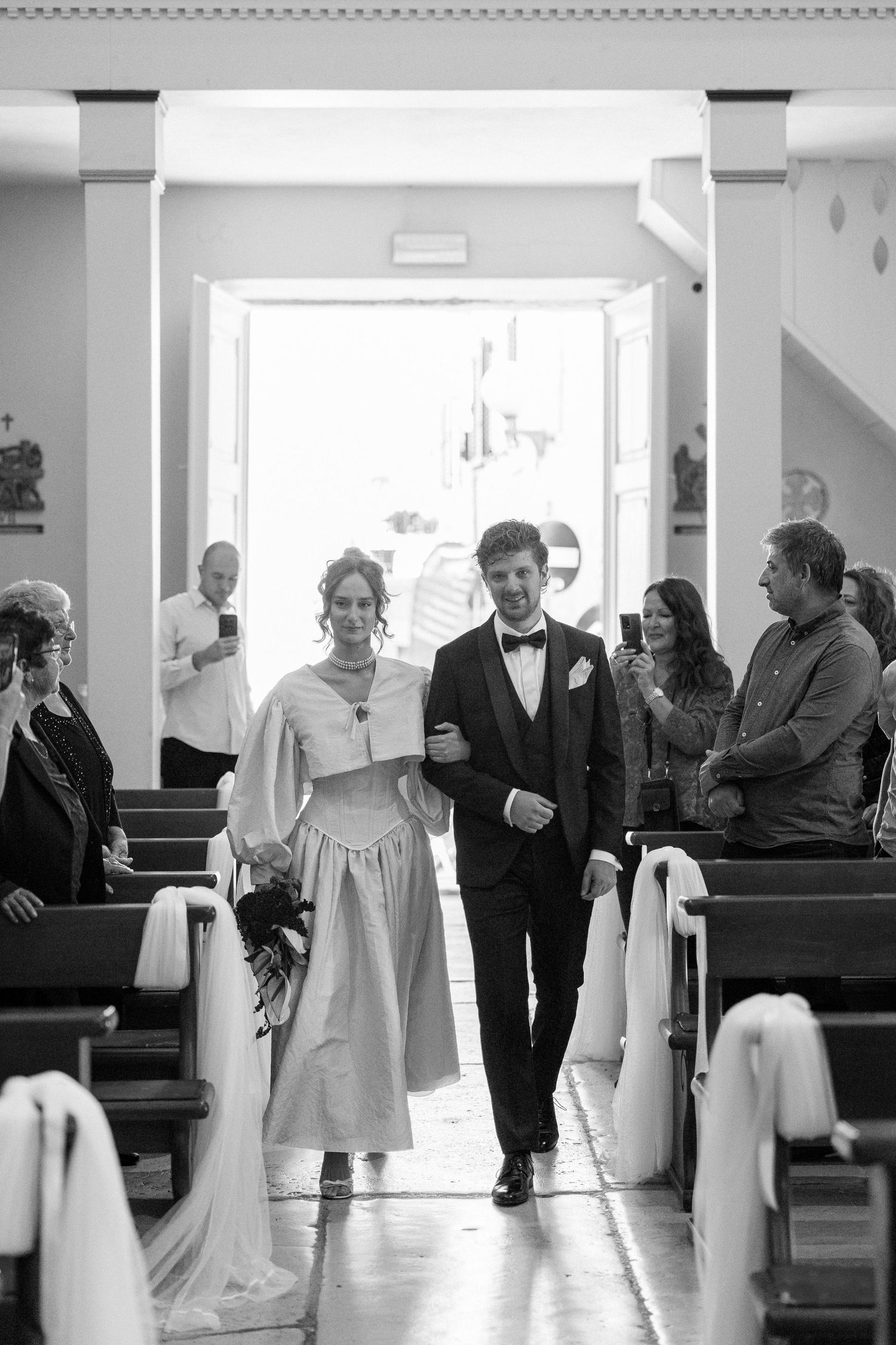 Wedding party members walking down church aisle in formal attire.