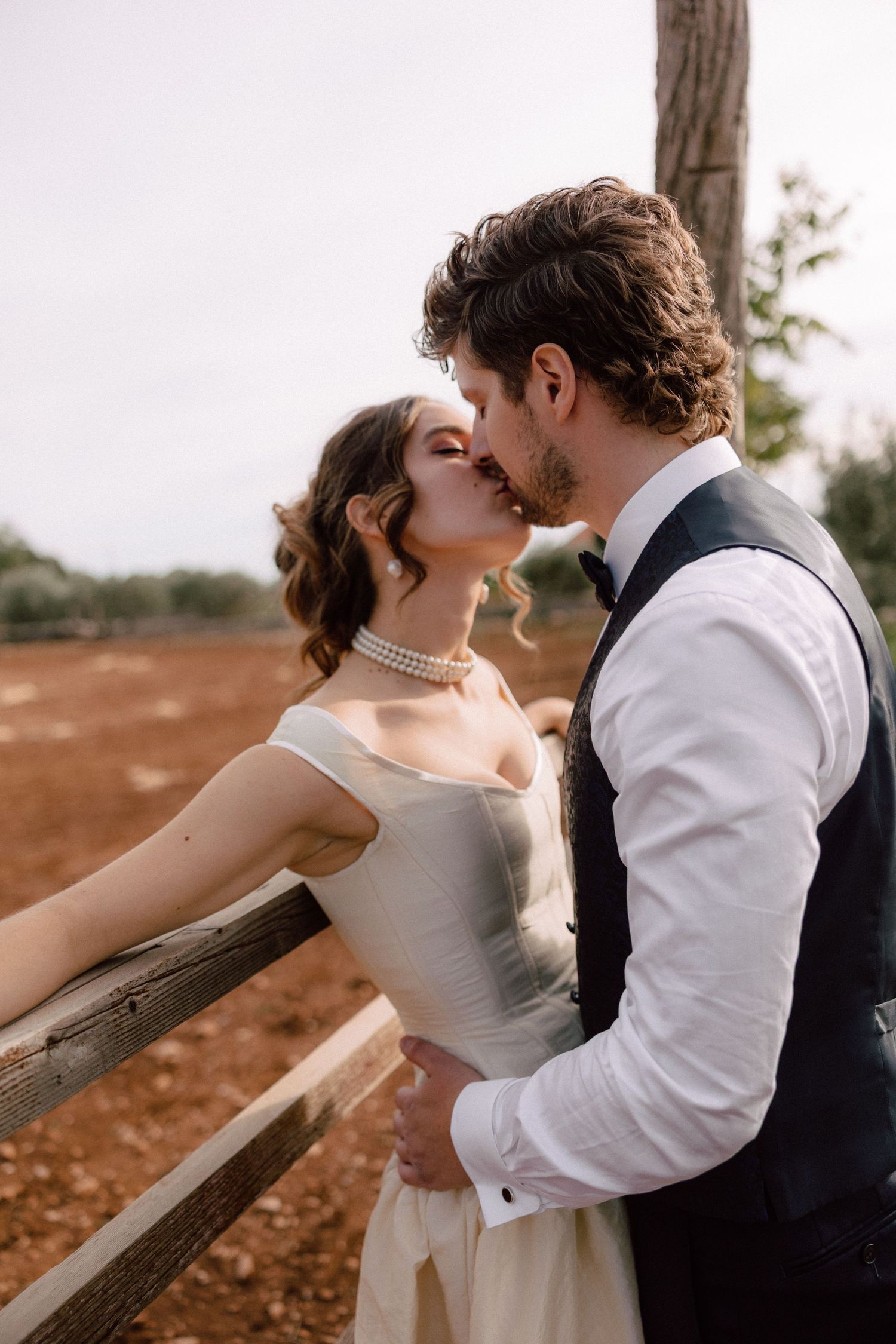 A romantic moment captured between newlyweds leaning against a wooden fence at sunset.