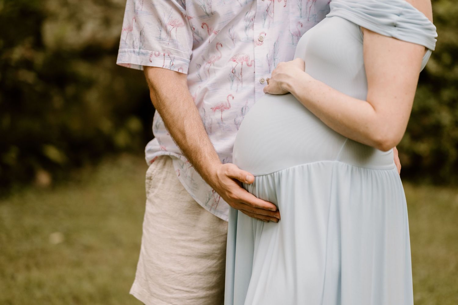 Intimate maternity photo showing couple's hands on baby bump outdoors.