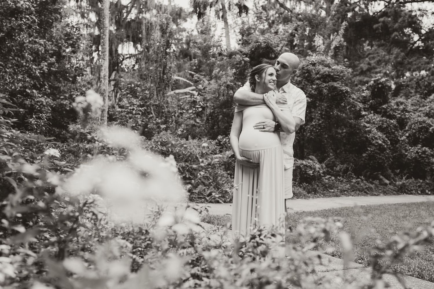 Romantic maternity photoshoot in a garden setting with flowing dress.