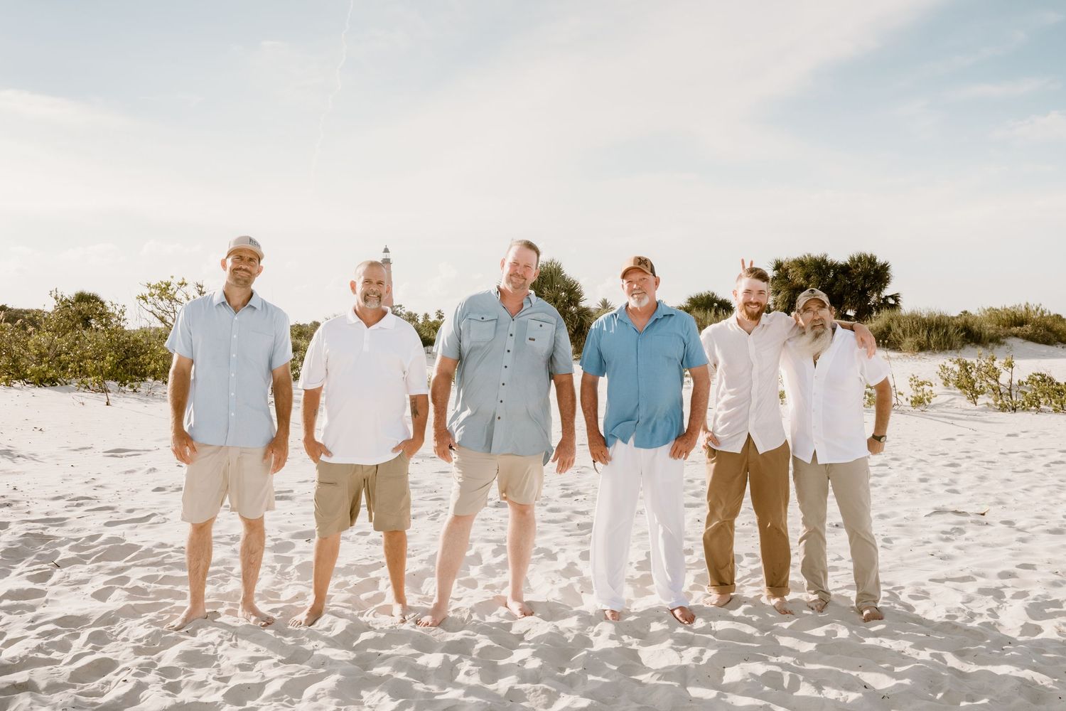 Wedding party members lined up on beach wearing coordinated blue and neutral colors.