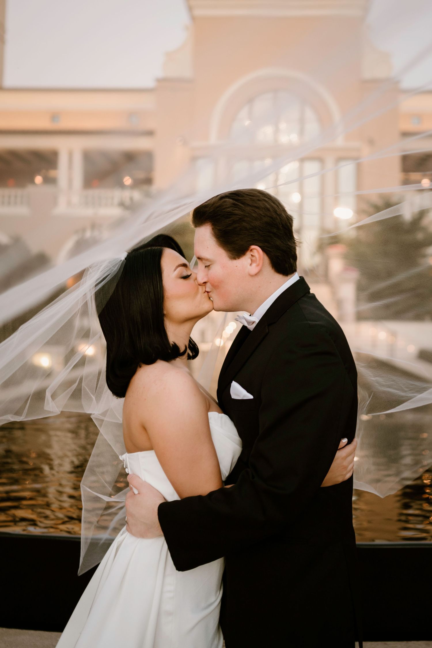 Intimate wedding portrait with flowing veil against sunset resort backdrop.