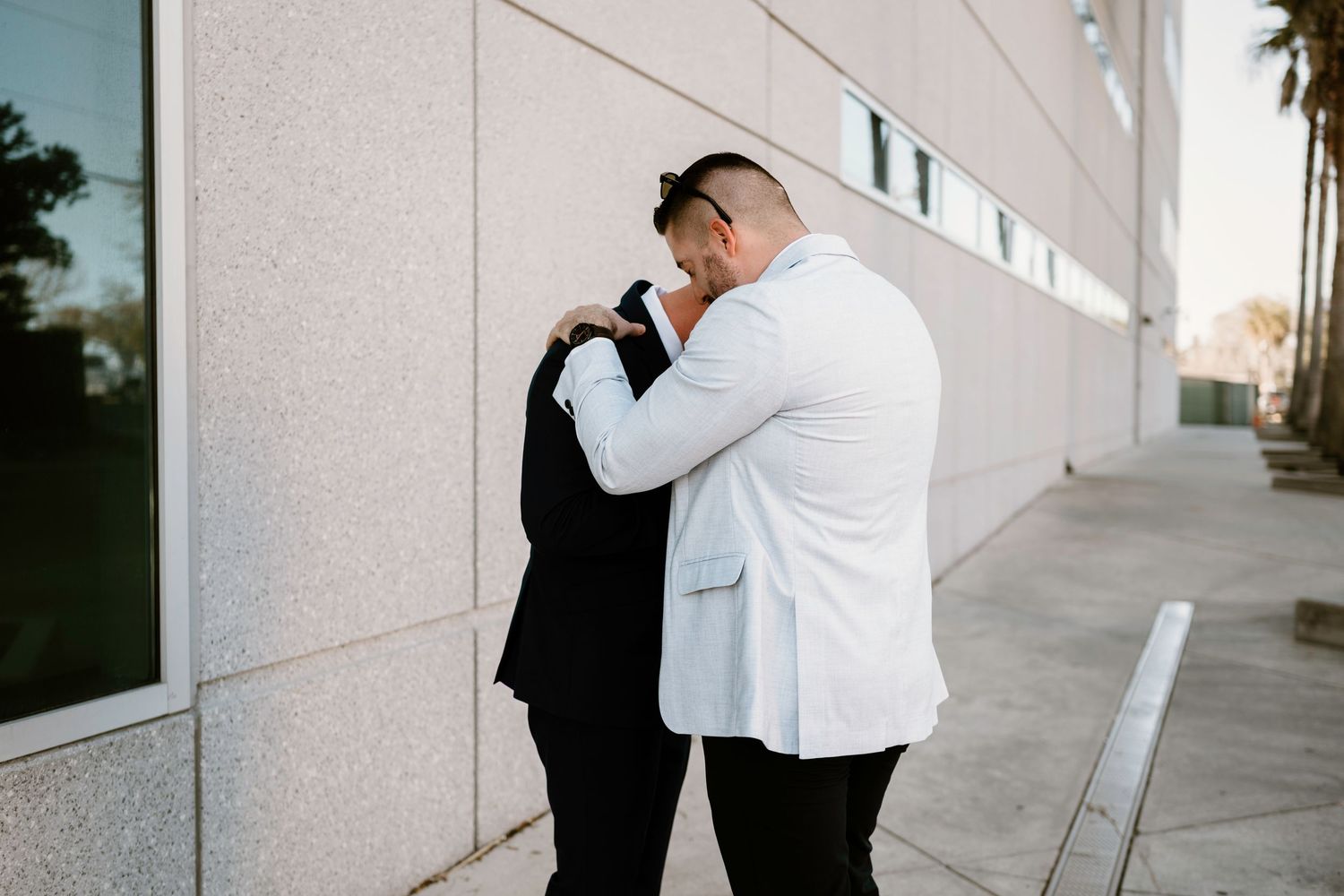 Couple embracing in formal attire during sunset outside a modern building.