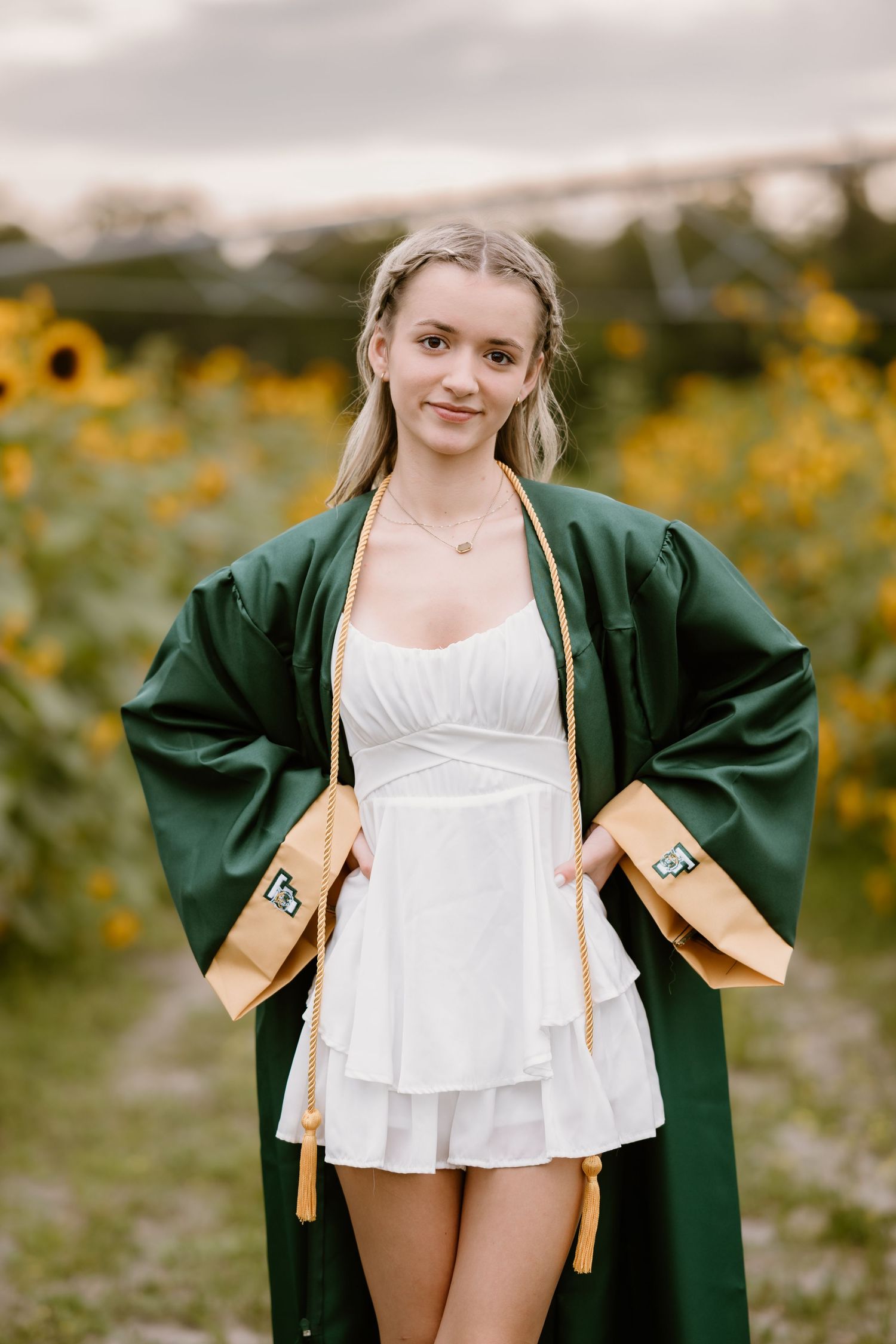 A graduation photoshoot featuring a green cap and gown with white dress in a sunflower field.