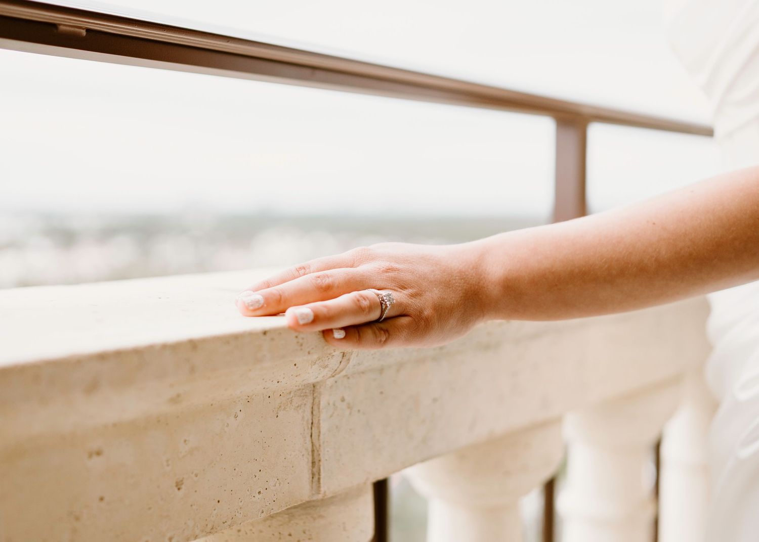Close-up of hands resting on ornate balcony railing in natural light.