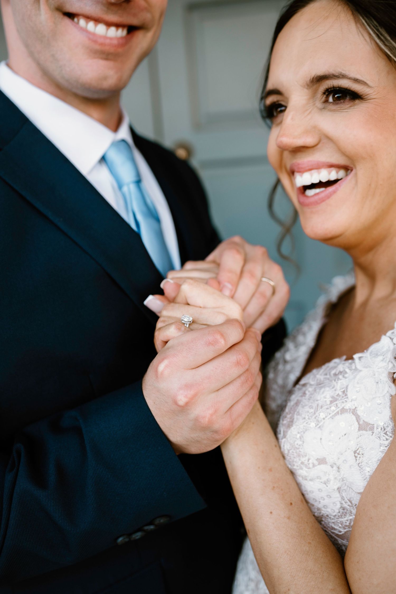 Close-up wedding photo showing couple holding hands with bride wearing white lace dress and groom in dark suit.