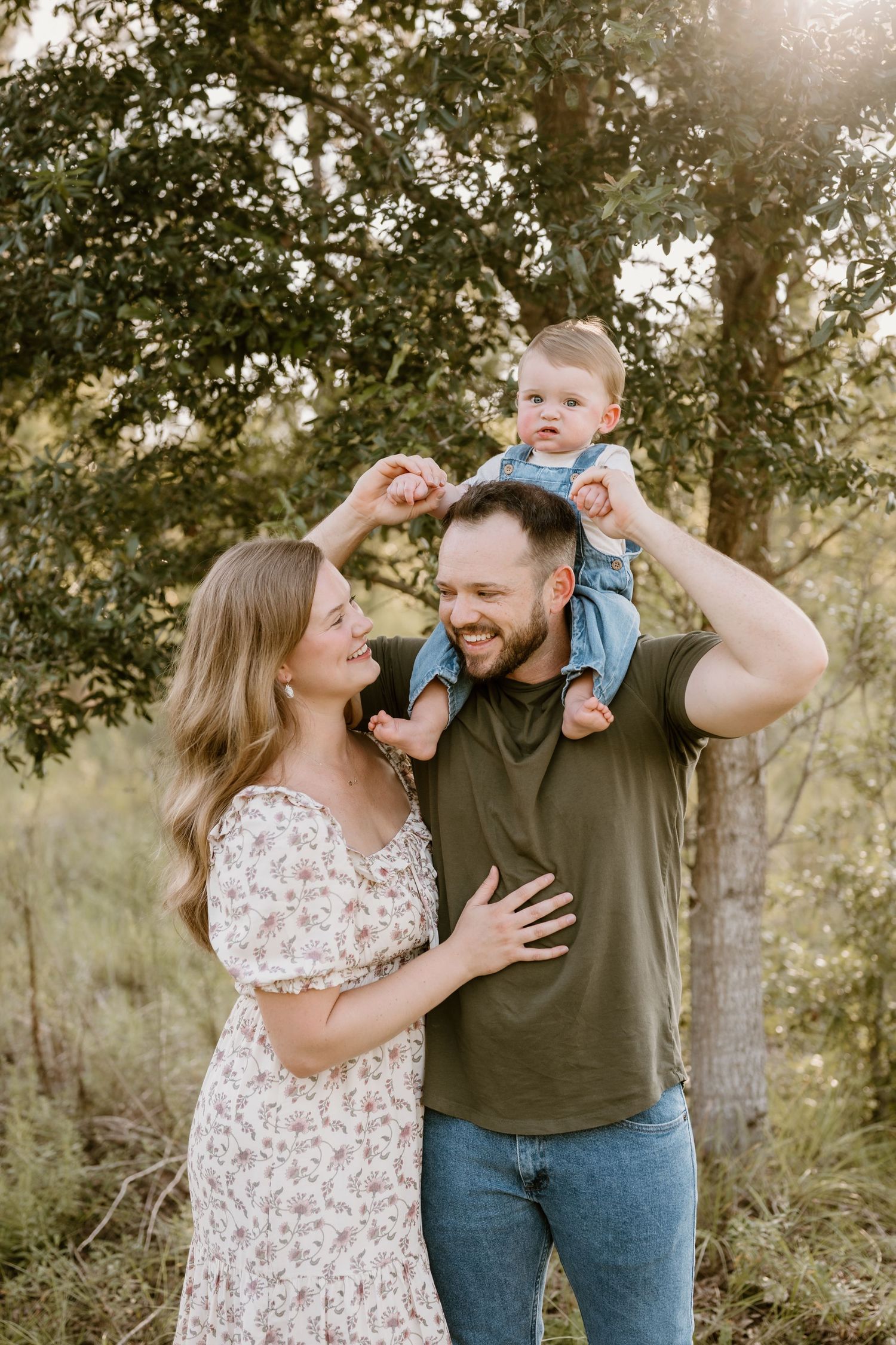 A couple plays with their baby in a natural outdoor setting during golden hour.
