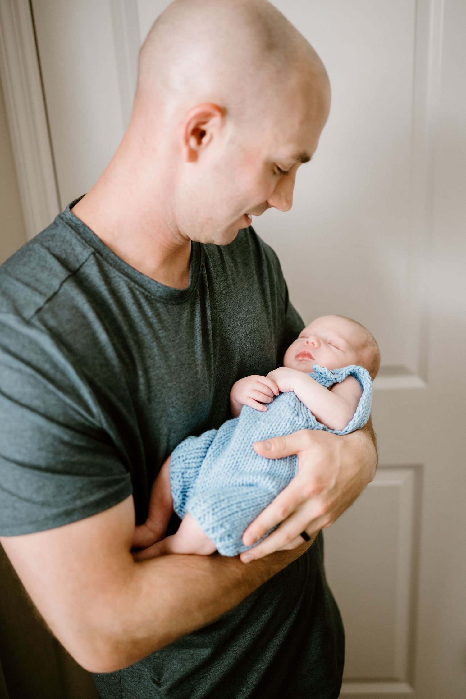 A baby wearing soft blue clothing is held securely in strong arms against a dark shirt.