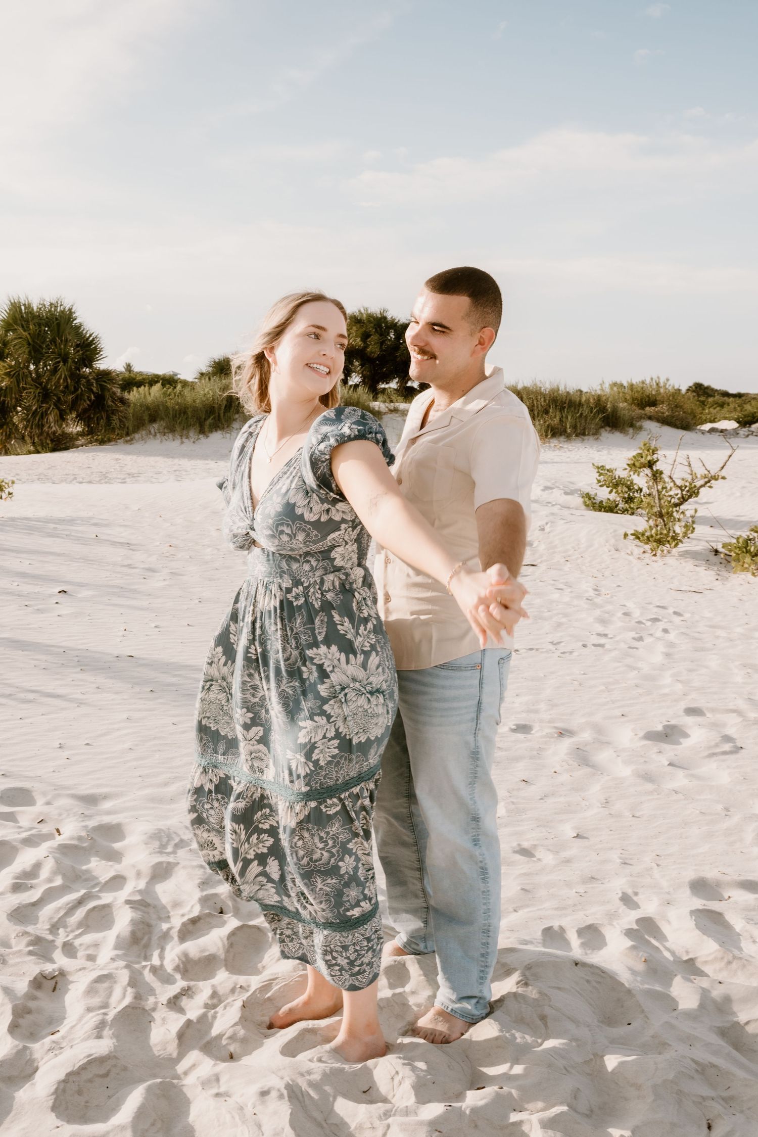 A couple dances playfully together on pristine white sand dunes during a sunny afternoon.