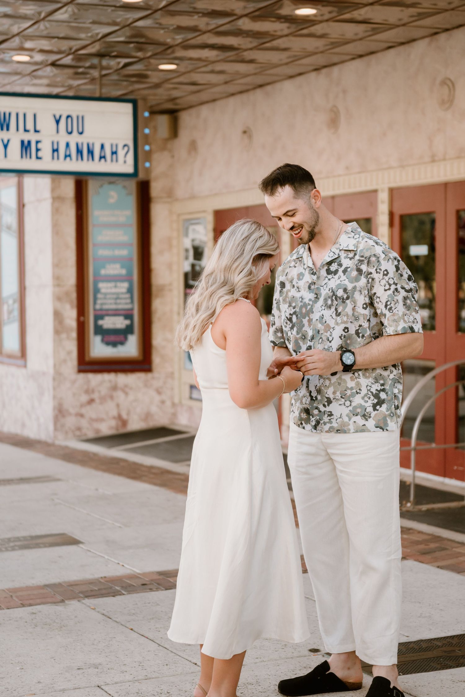 A marriage proposal scene unfolds at a retro movie theatre entrance.