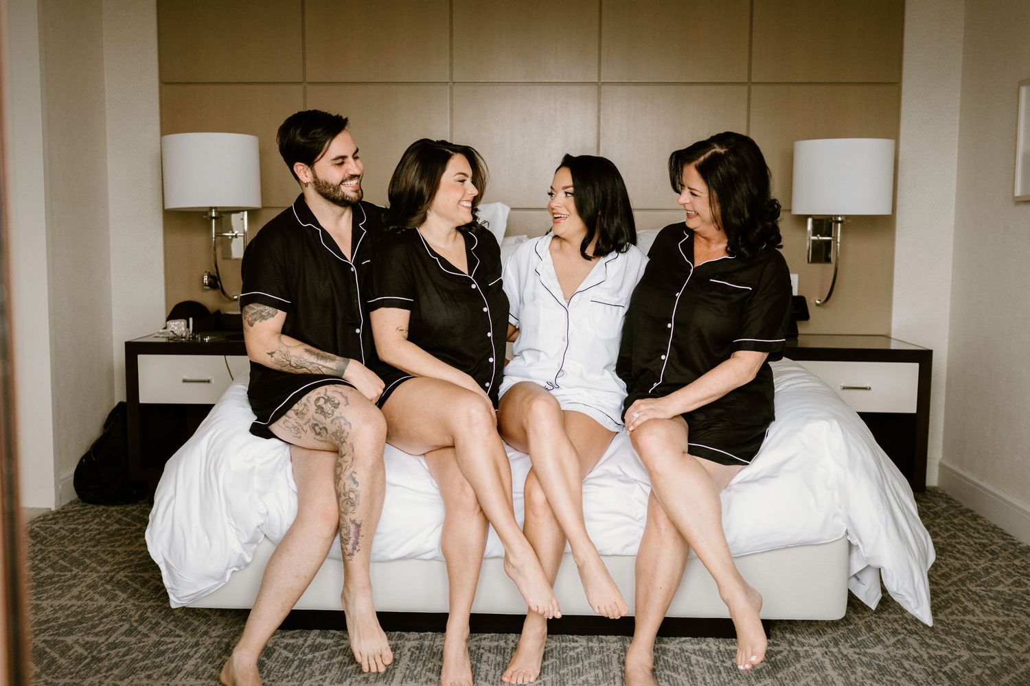 Group of friends in black and white outfits lounging on a hotel bed together.