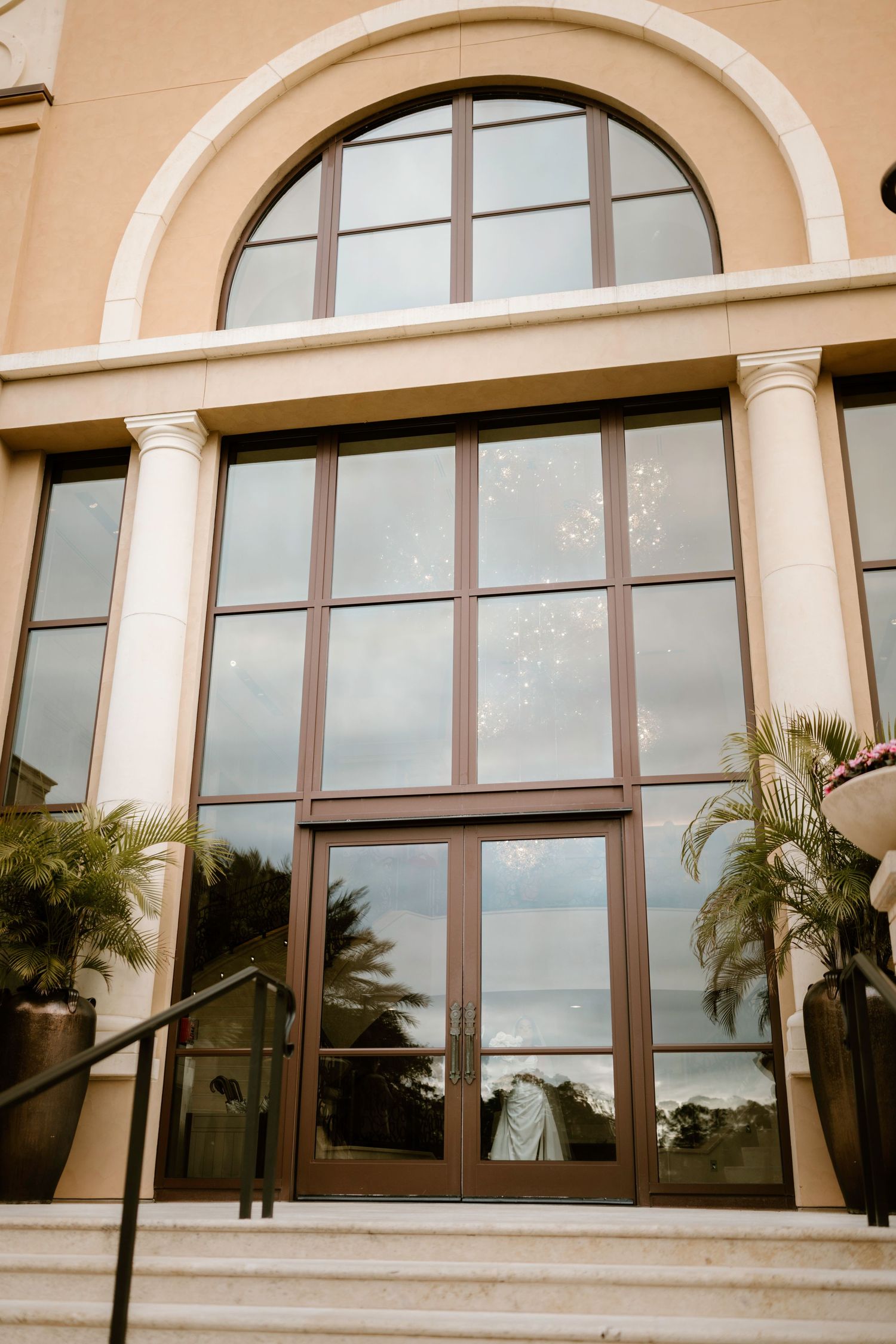 Elegant beige building exterior with arched windows, columns and palm trees framing the entrance.