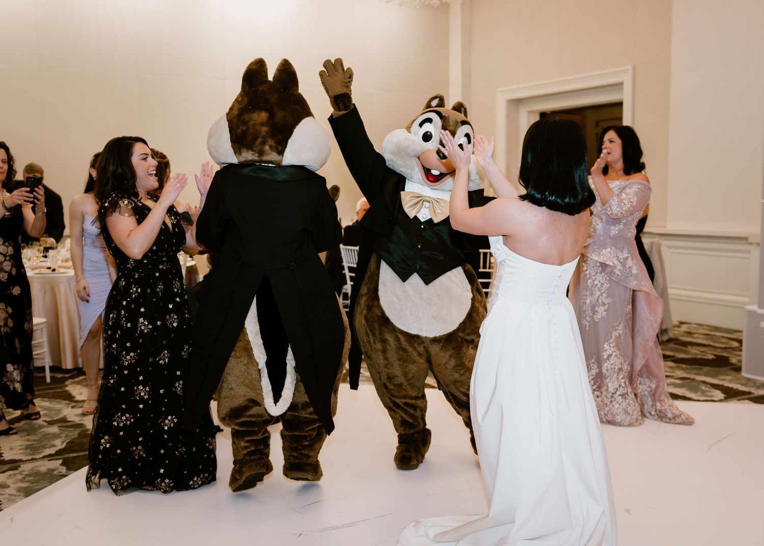 Wedding guests and Disney mascot characters dance together at an elegant reception.