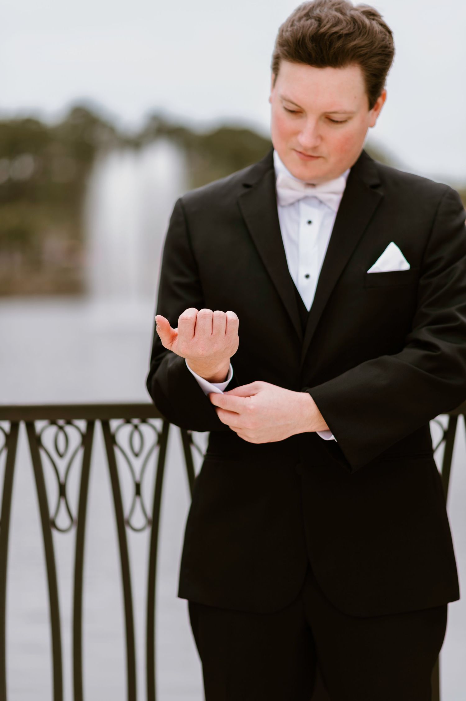 Groom in black tuxedo adjusting cufflinks before ceremony.