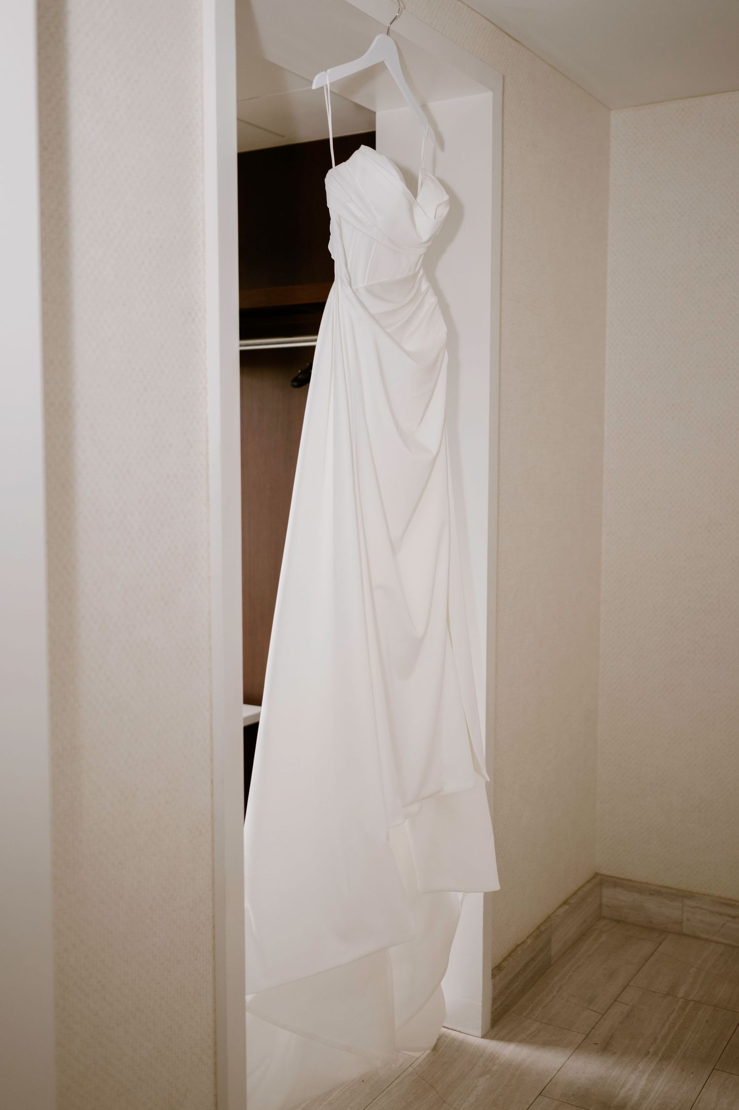 A white wedding dress hanging in a closet with draped fabric and clean lines.
