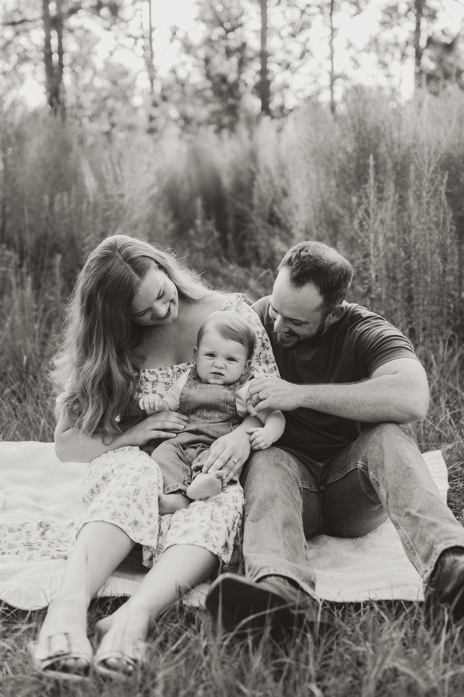A black and white photo series of a family lying on a blanket in a grassy field.