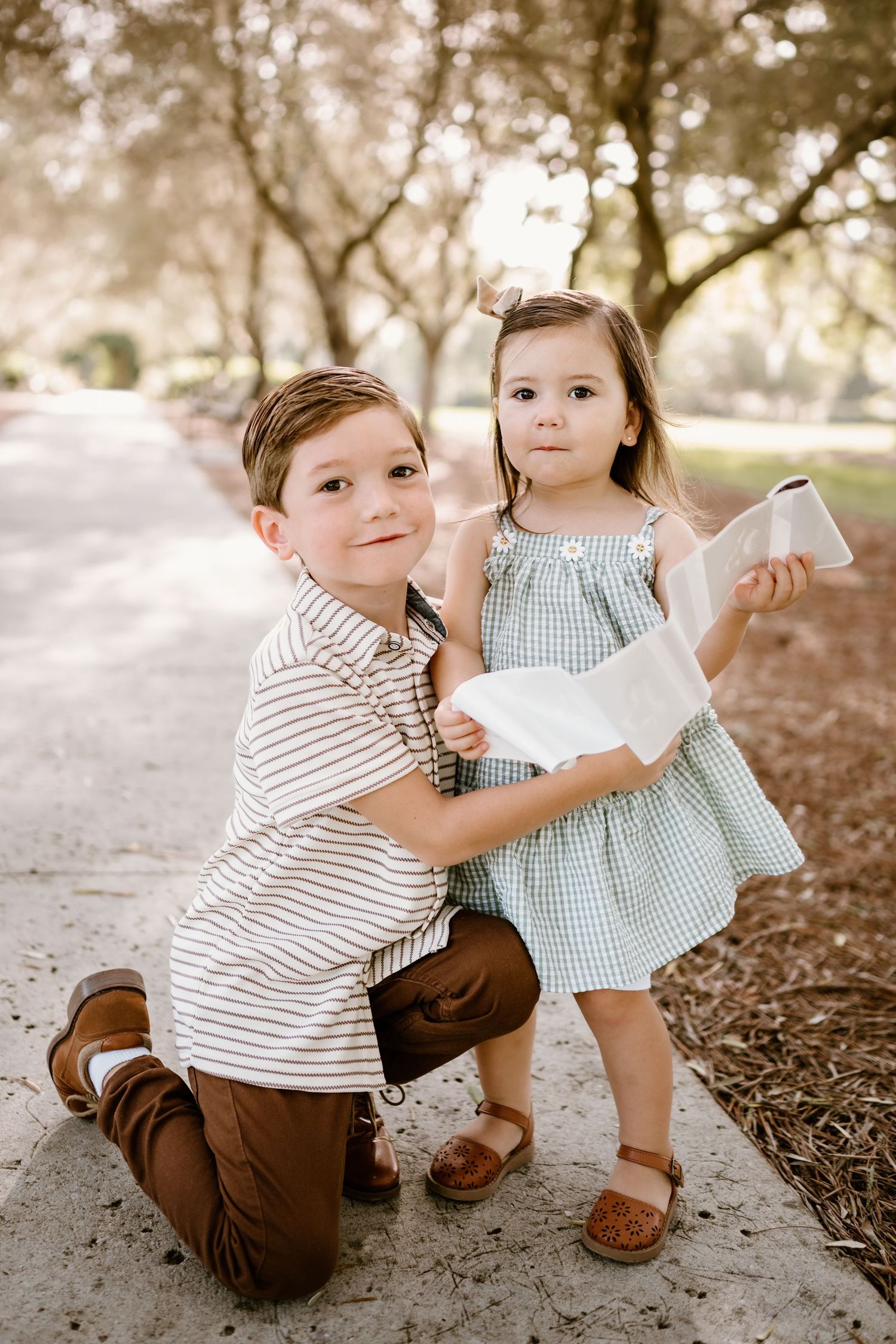 Two small children playing together on the ground in casual clothing during an outdoor photo session.